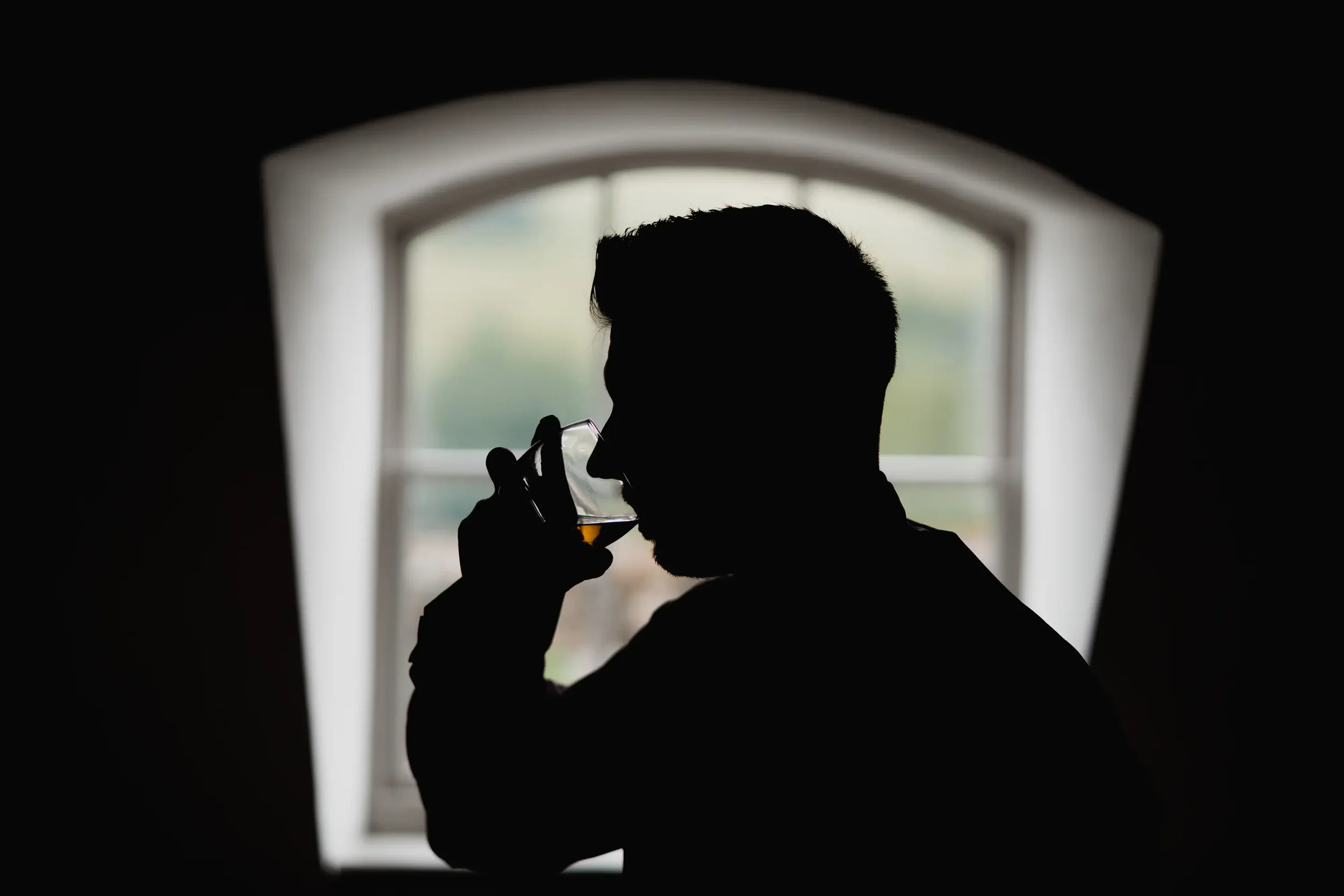 Silhouette of a man drinking from a glass, with a window in the background
