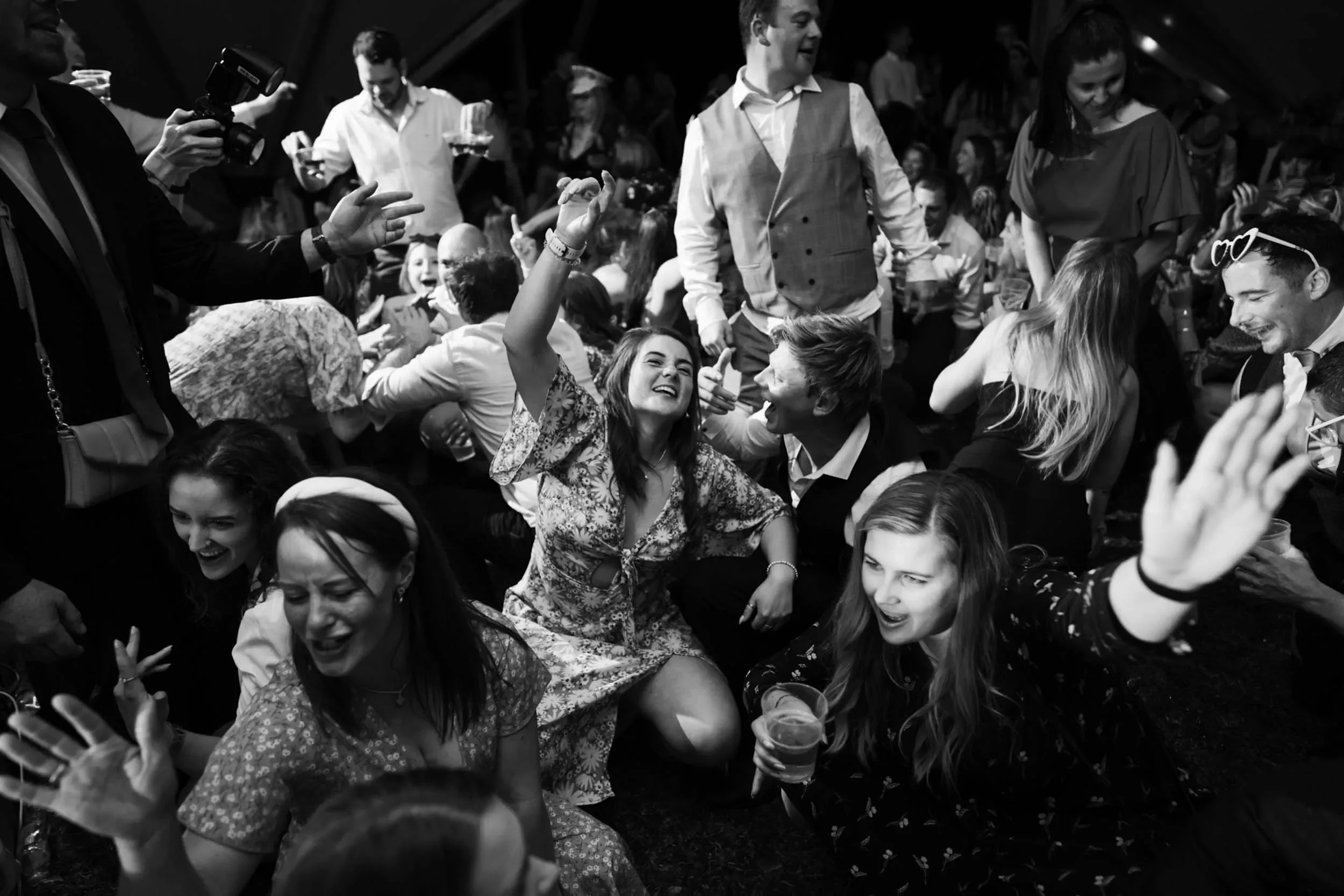 People dancing, laughing, and having fun at a lively party or celebration, with some holding drinks, in a crowded indoor setting.
