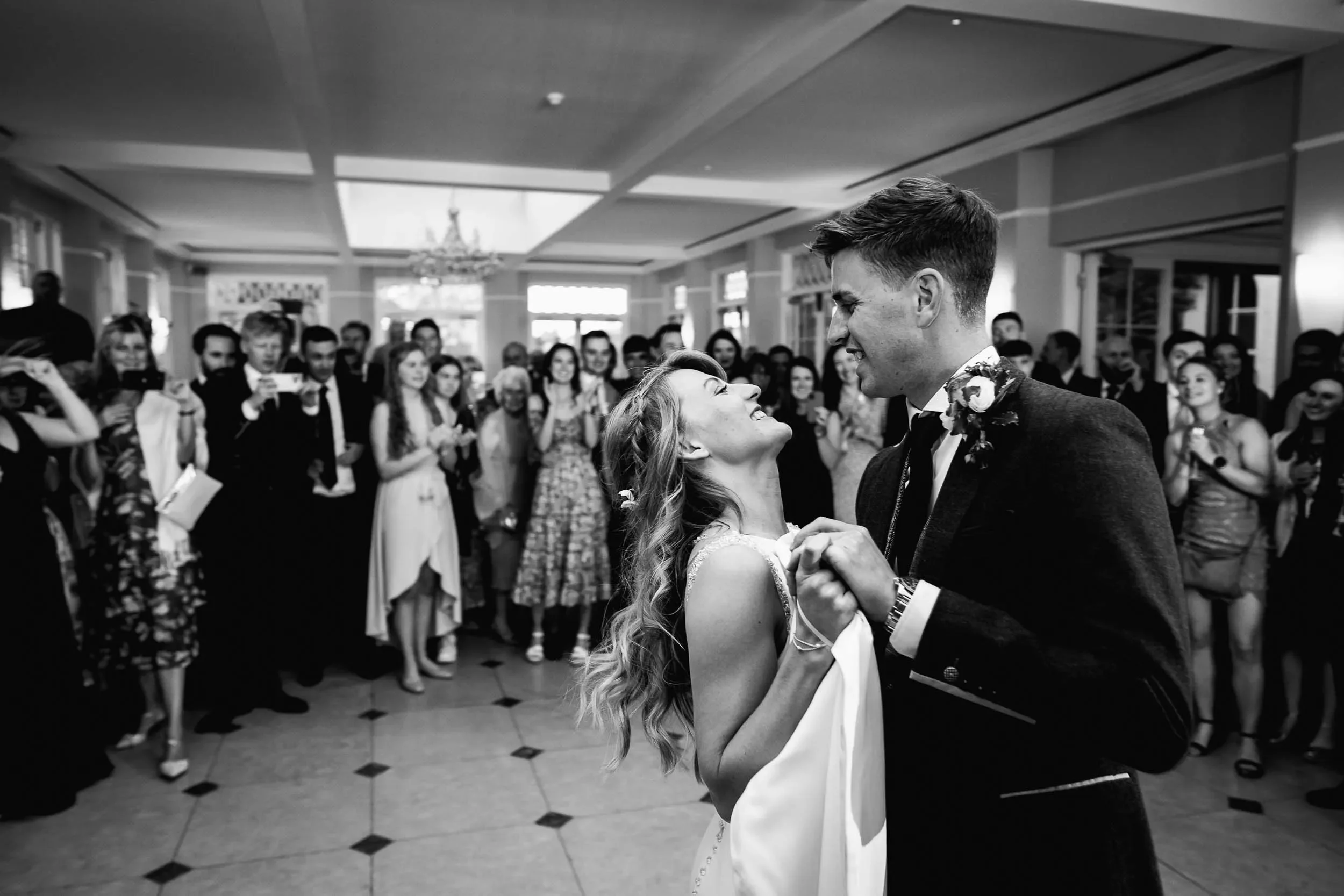 A bride and groom share their first dance at their wedding reception, surrounded by friends and family in a decorated banquet hall.