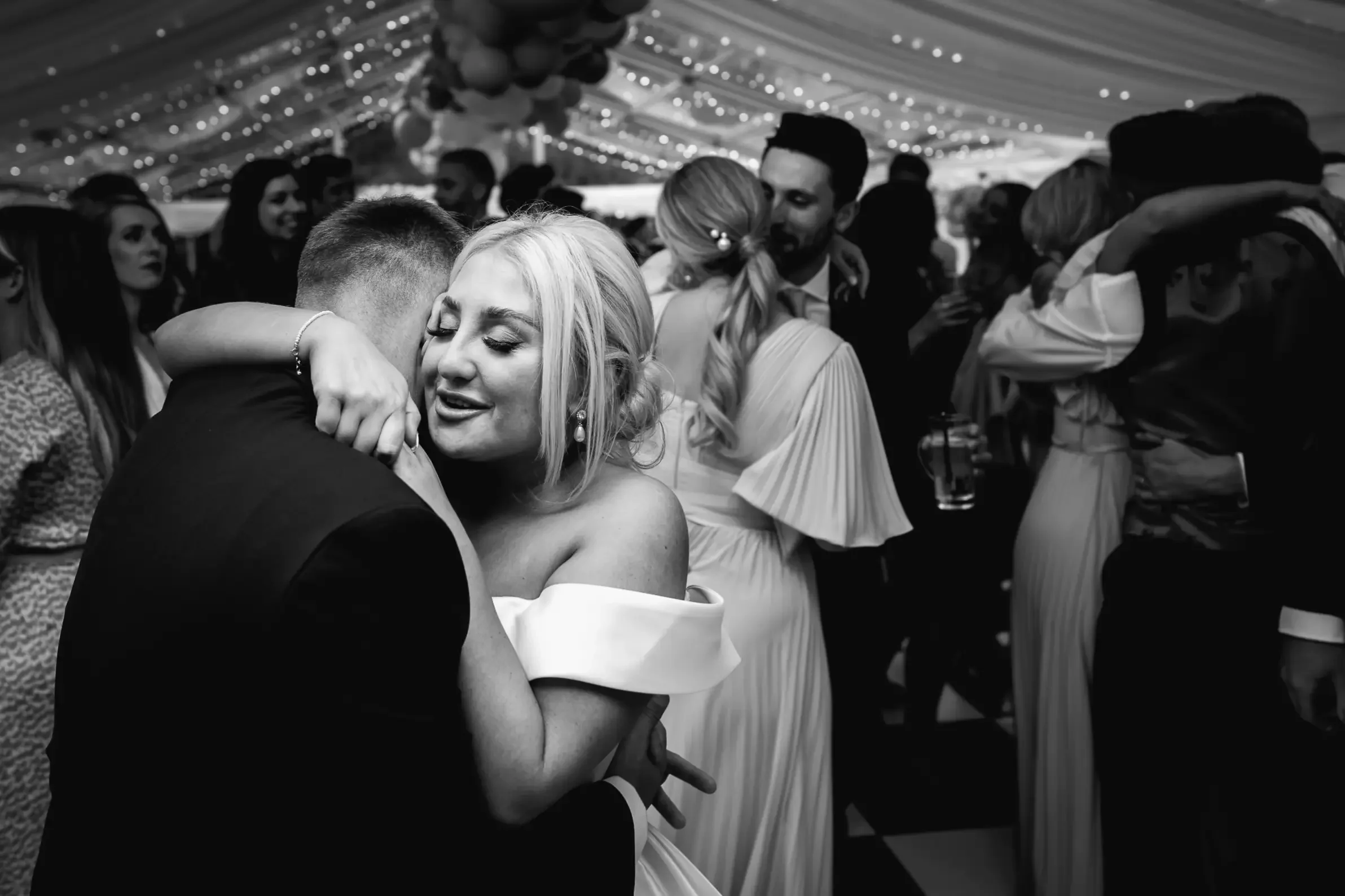 Black and white photo of couples dancing at a wedding reception, embracing and smiling.
