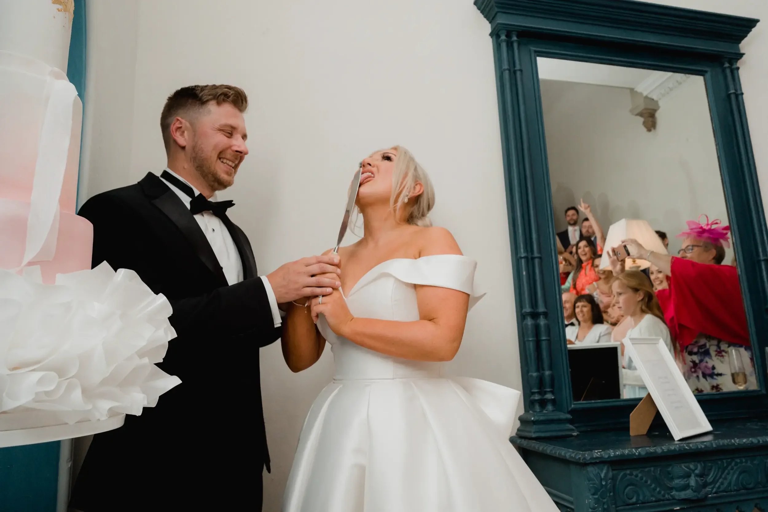 Bride and groom at their wedding, bride playfully sticking out her tongue and audience taking photos