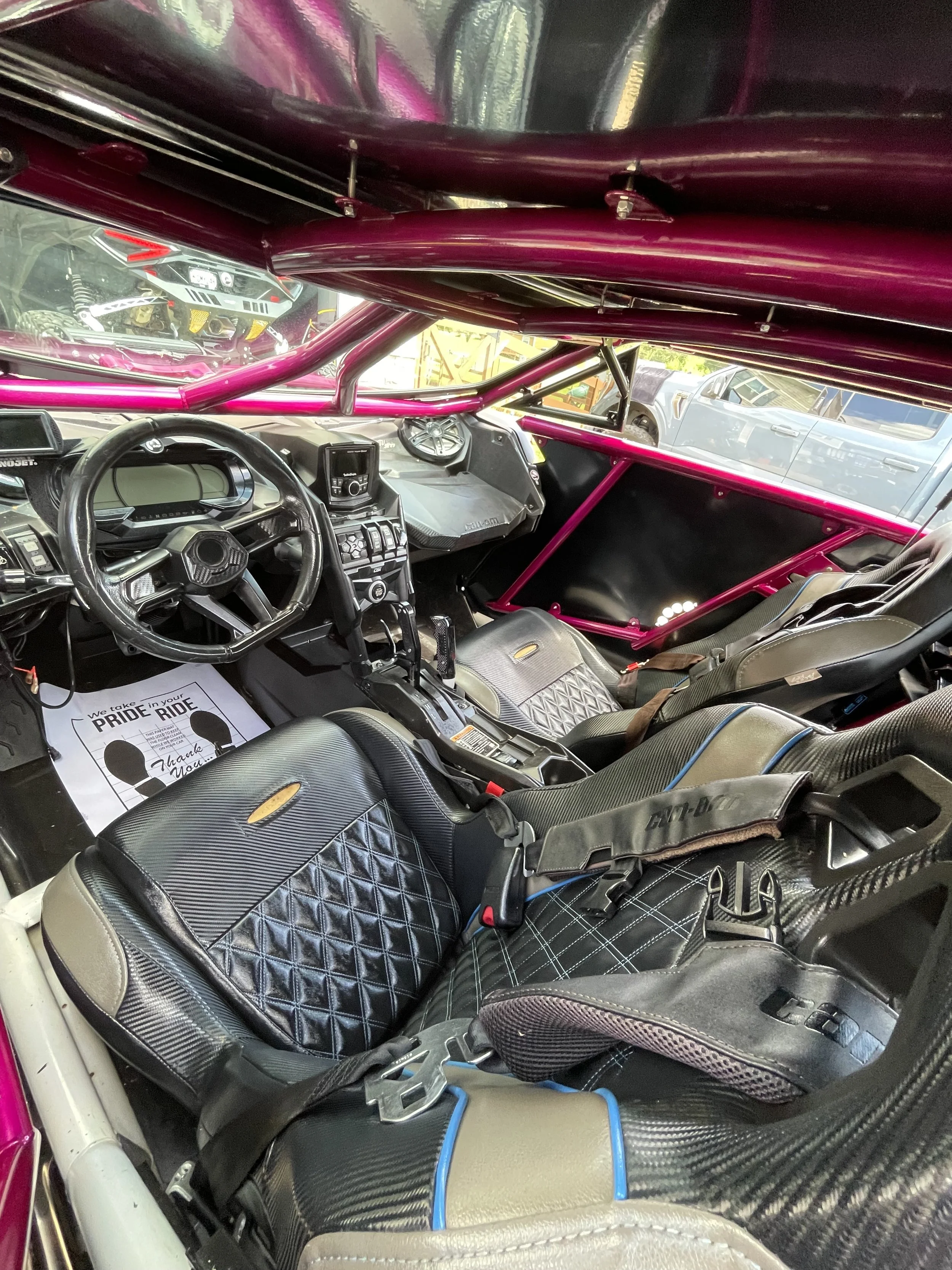 Interior of a race car with black and beige leather seats, a digital dashboard, and a pink roll cage.
