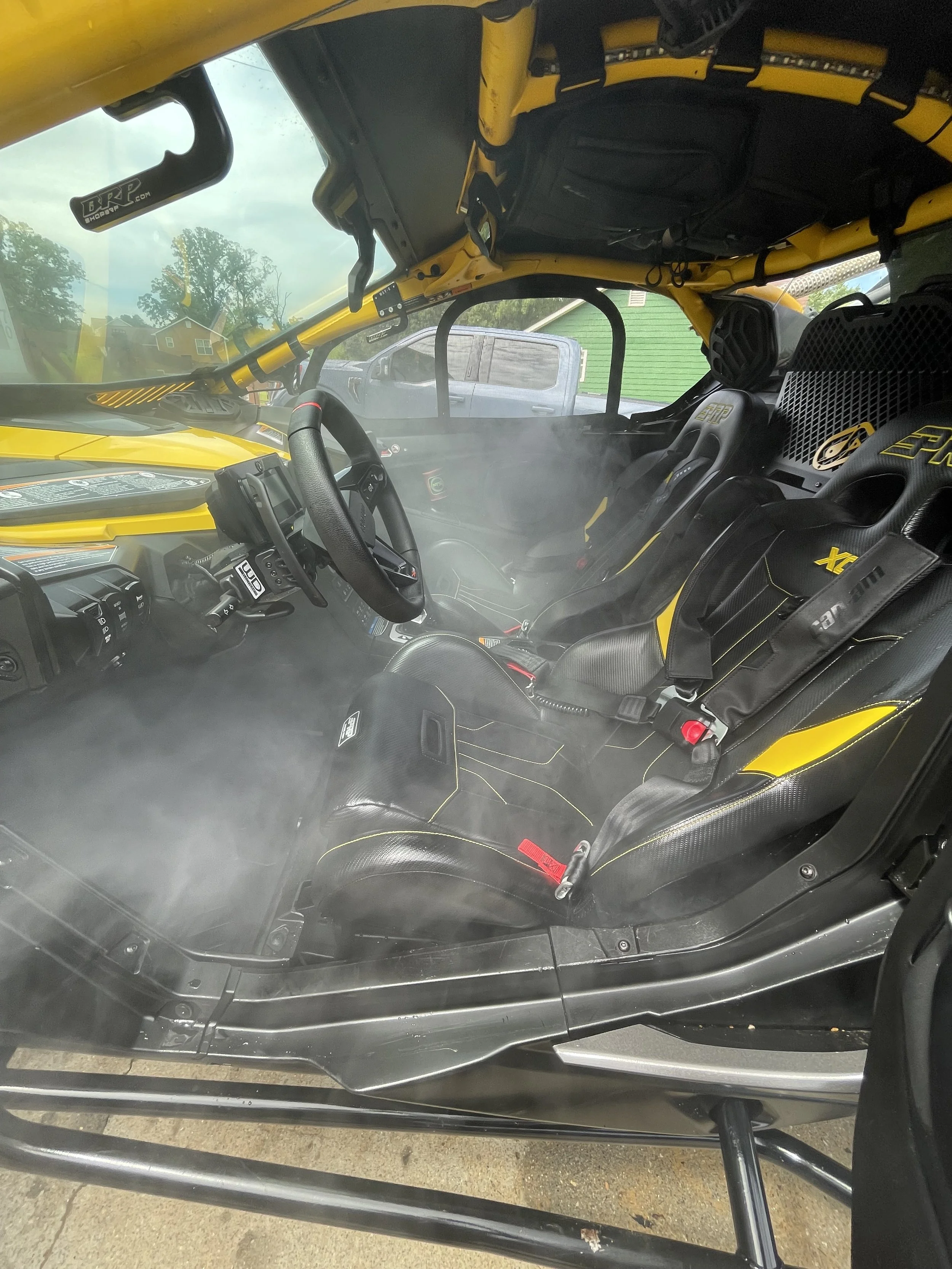Inside view of a yellow off-road vehicle with two racing seats and a steering wheel, seen through a window with fog or mist inside.