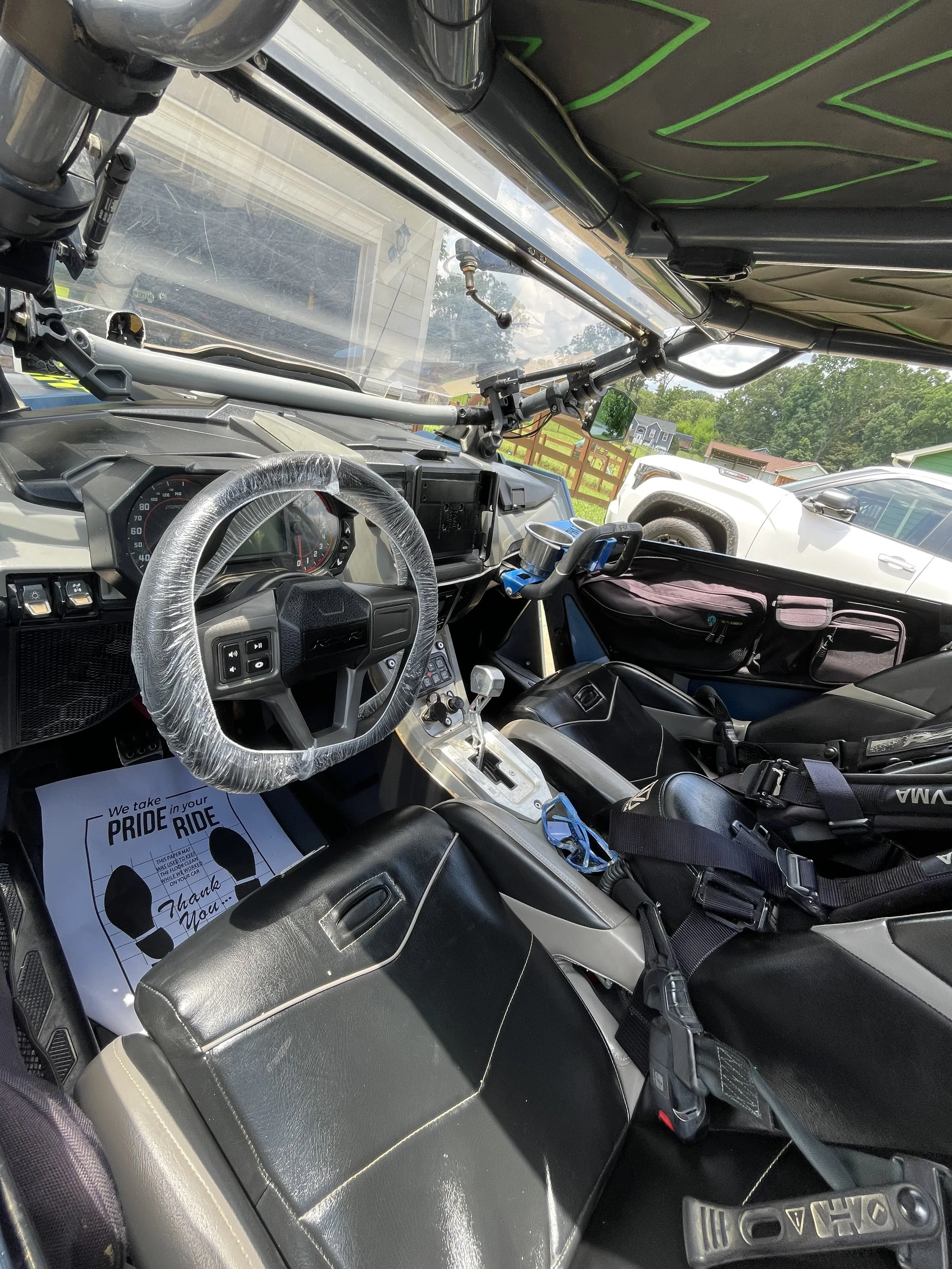Inside the cockpit of a police or emergency vehicle, showing a steering wheel with a plastic cover, control panel, and seating area with seat belts. There is a paper on the floor that thanks for taking the pride ride.