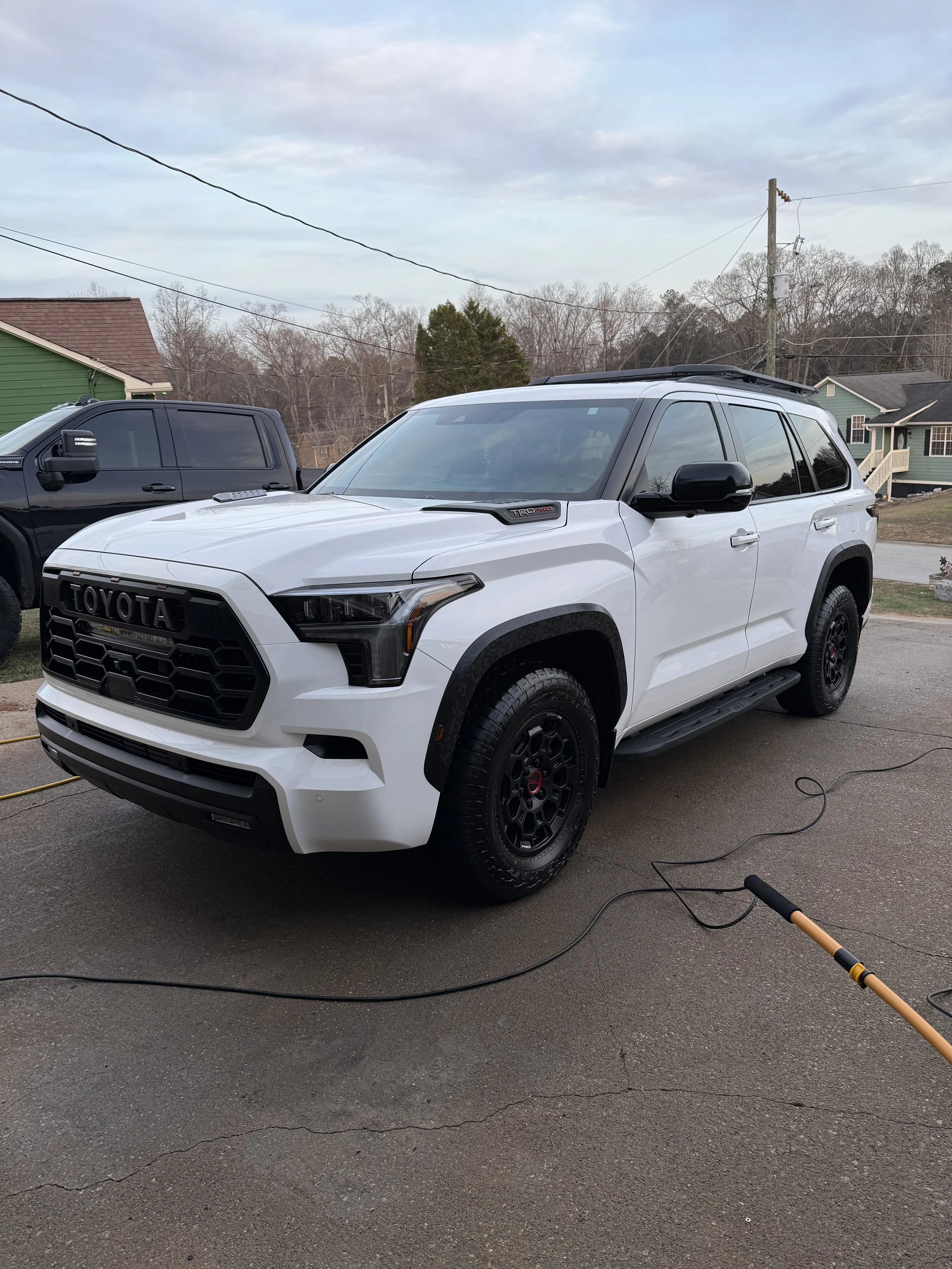 White Toyota SUV parked on a driveway during daytime, with a black vehicle behind it and houses in the background.