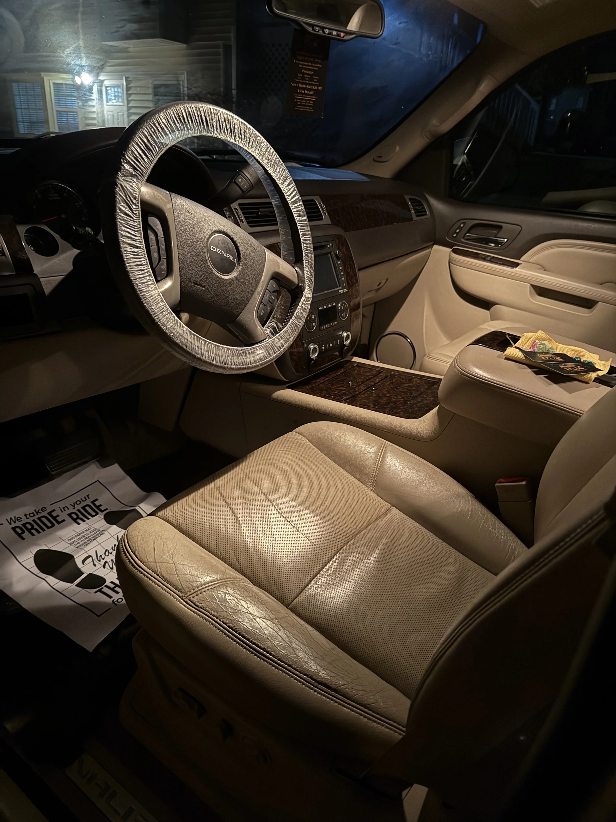 Interior of a beige leather seat car with a wood grain dashboard and a steering wheel with a plastic cover.