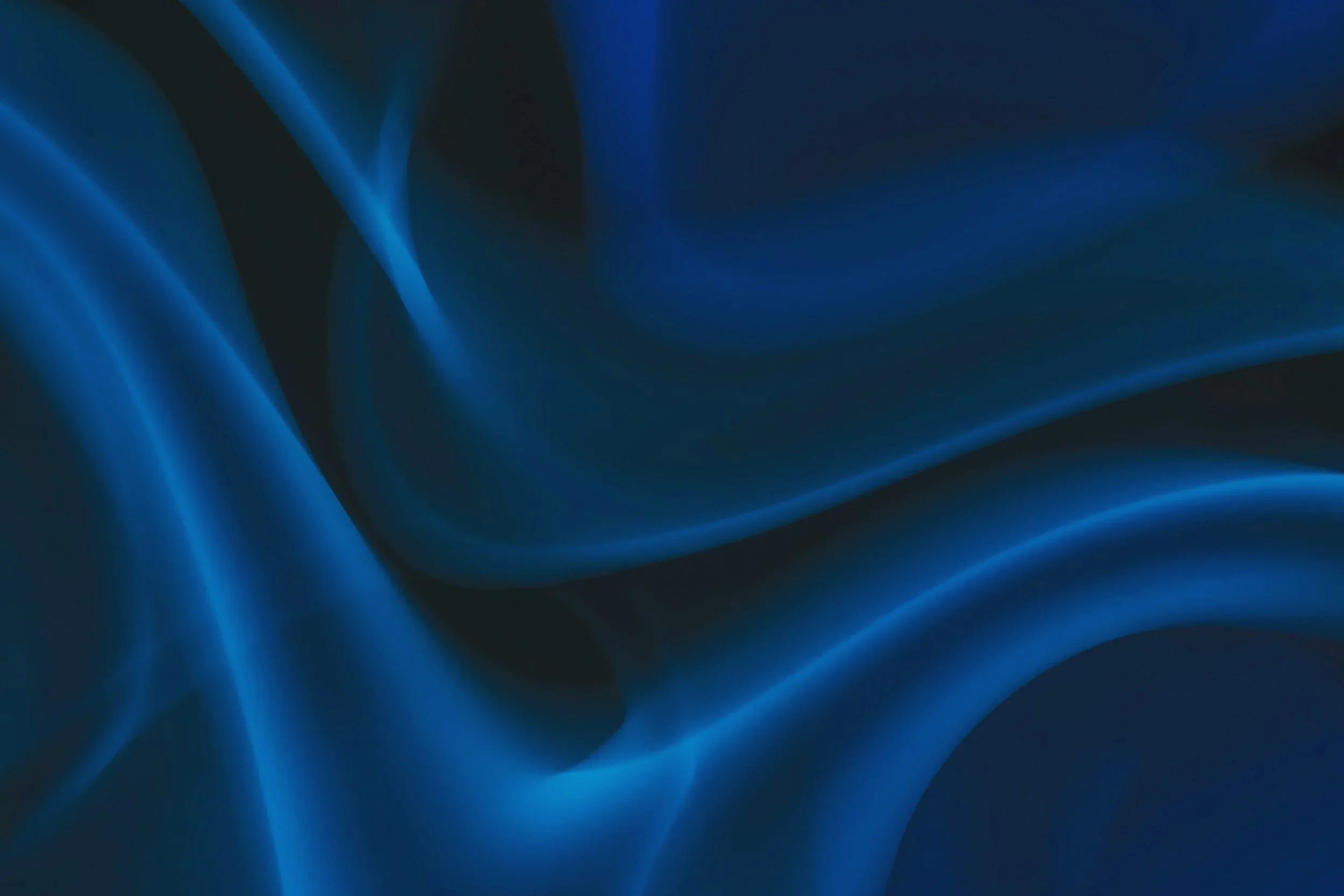 Abstract image of flowing dark and bright blue silk-like fabric with smooth curves and glossy surface.