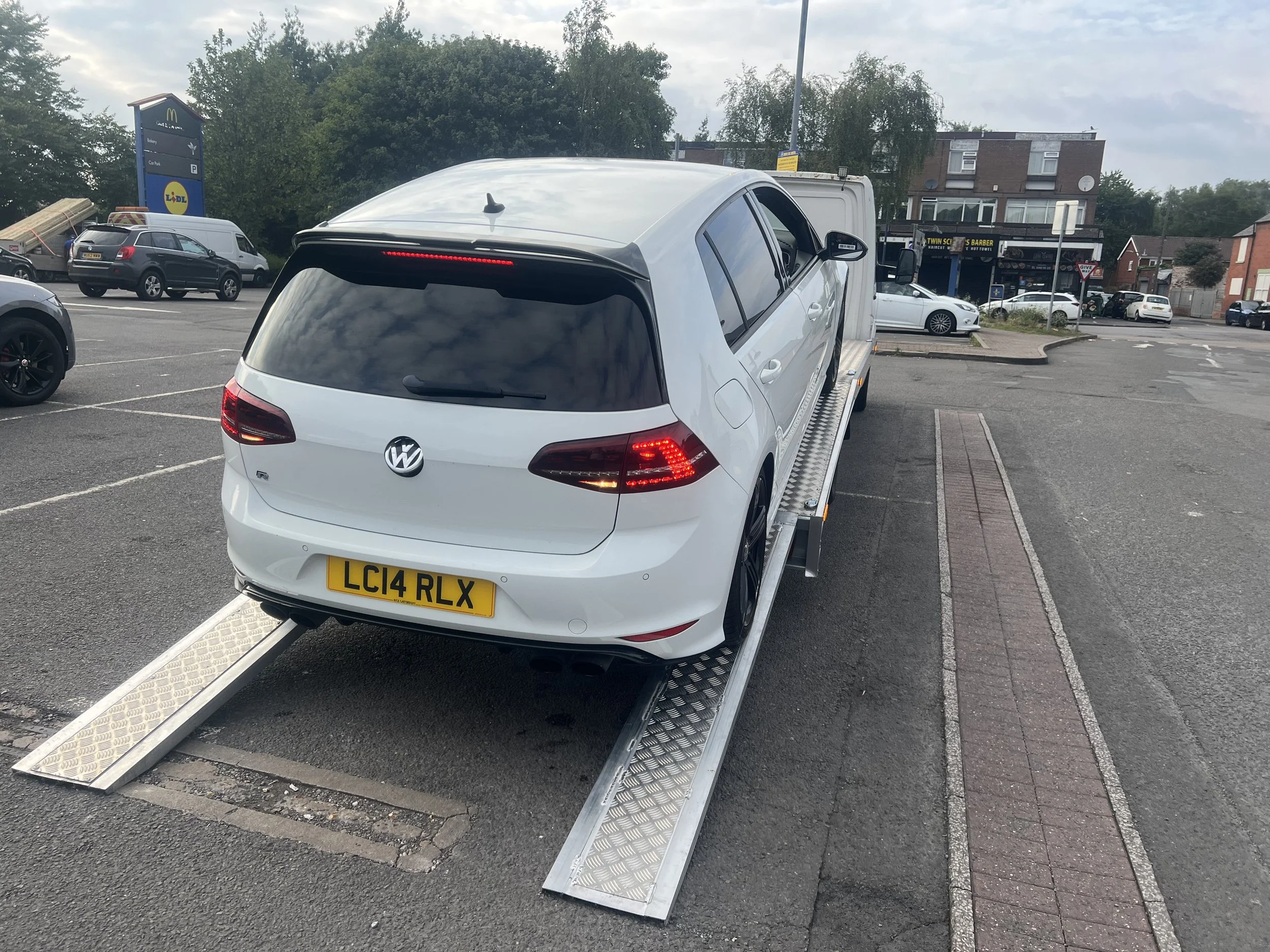 White Volkswagen car on a vehicle lift in a parking lot.