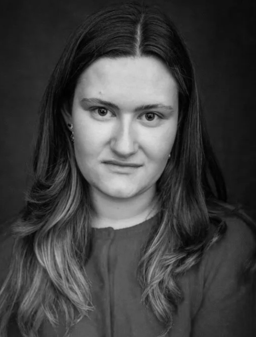 Black-and-white portrait of a young woman with long, wavy hair, looking directly at the camera with a neutral expression.