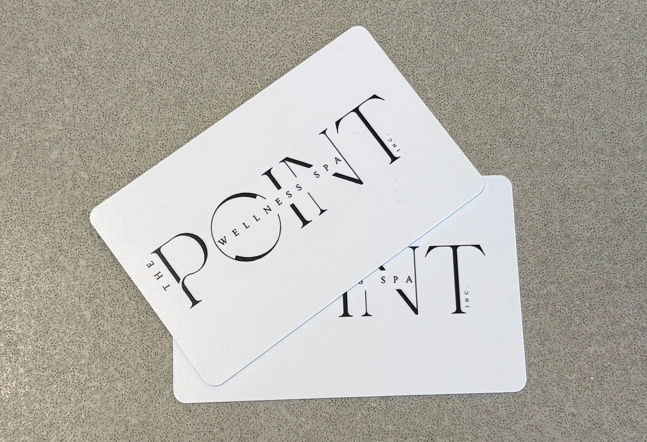 Two white membership cards for The POINTE Wellness Spa on a gray surface.