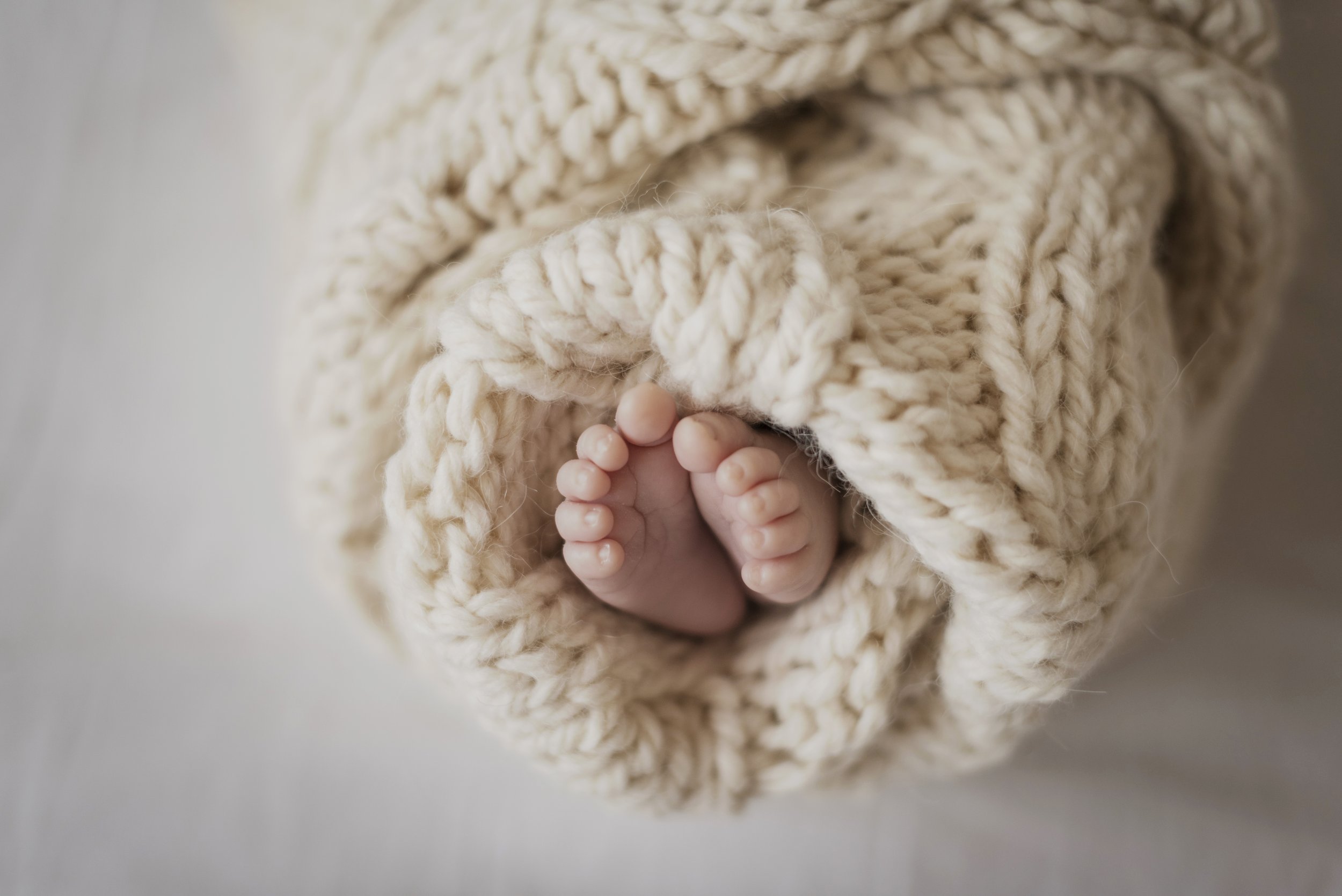 Close-up of tiny baby toes wrapped in a soft, chunky beige knit blanket.