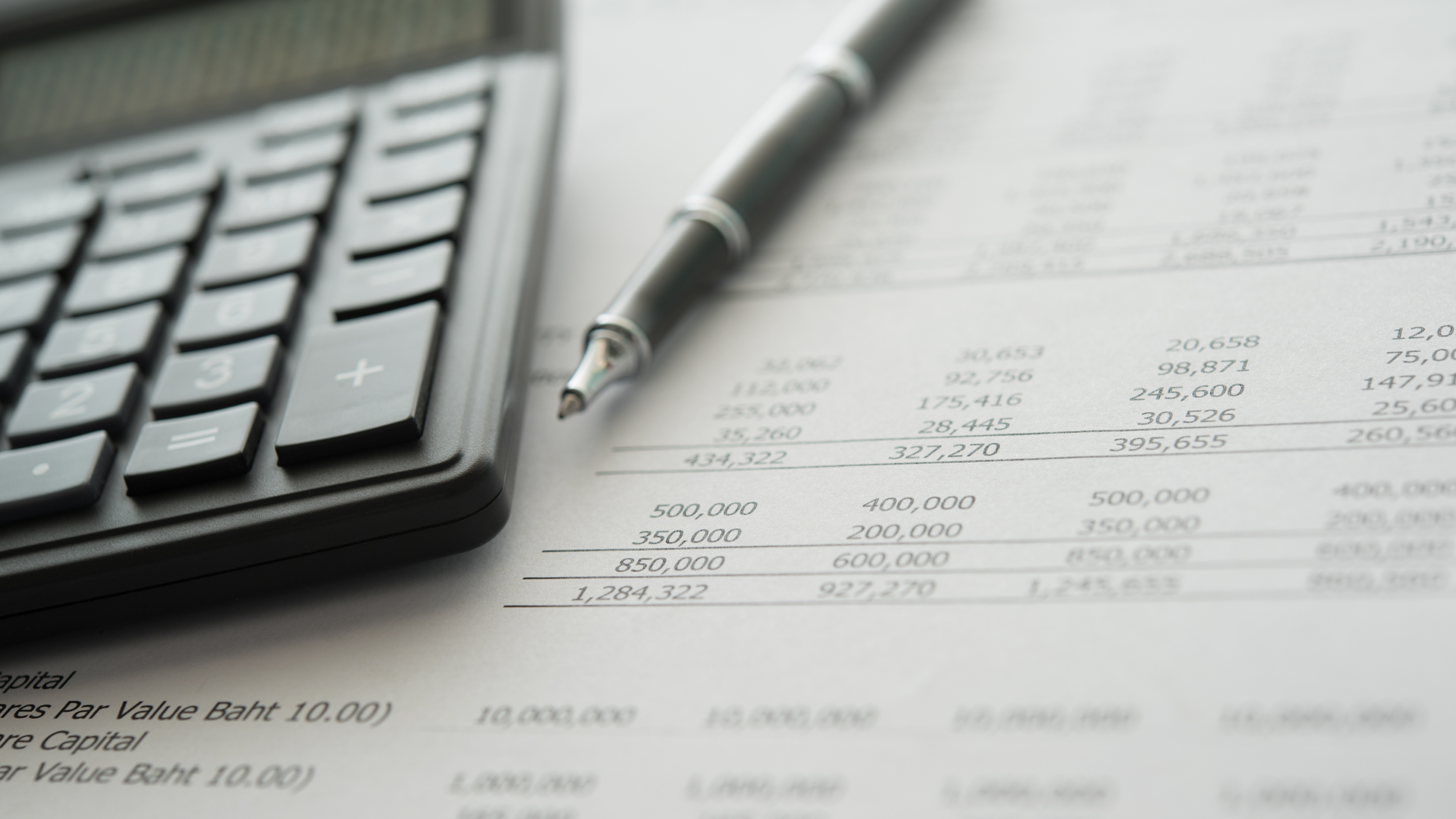 Close-up of a calculator, a pen, and a financial document with numerical data and calculations.