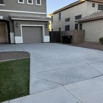 Empty residential driveway with adjacent lawn and houses in the background.