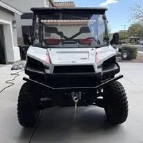 Front view of a black and white off-road utility vehicle with large tires parked on a driveway.
