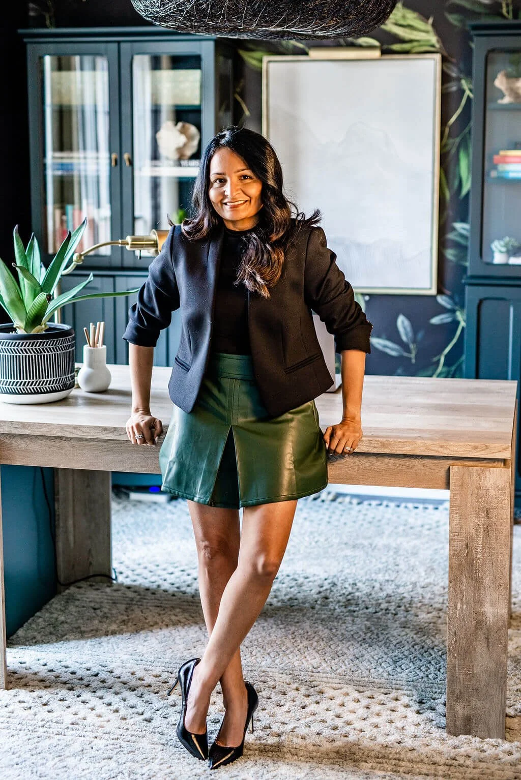 Jasmine Shah, founder of The Velvet Finch, smiling in a navy blazer and green skirt in a stylishly designed studio