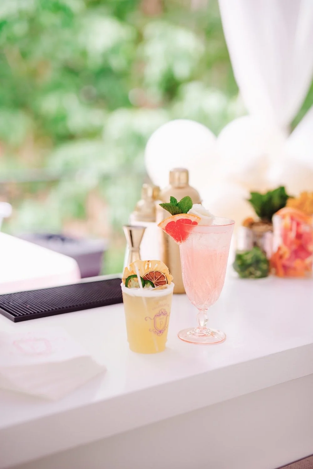 Close-up of two signature cocktails garnished with grapefruit slices and mint, served in custom branded cups alongside gold bar shakers