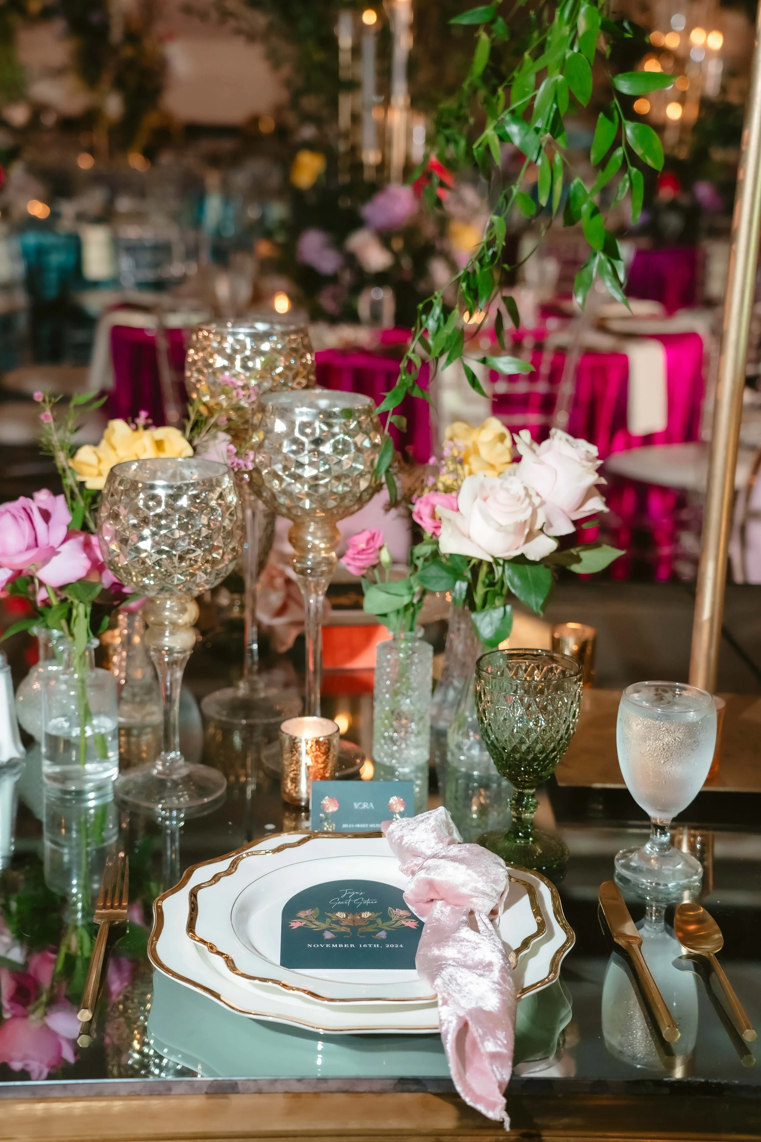 Elegant wedding tablescape with jewel-toned glassware, pink roses, and custom place settings
