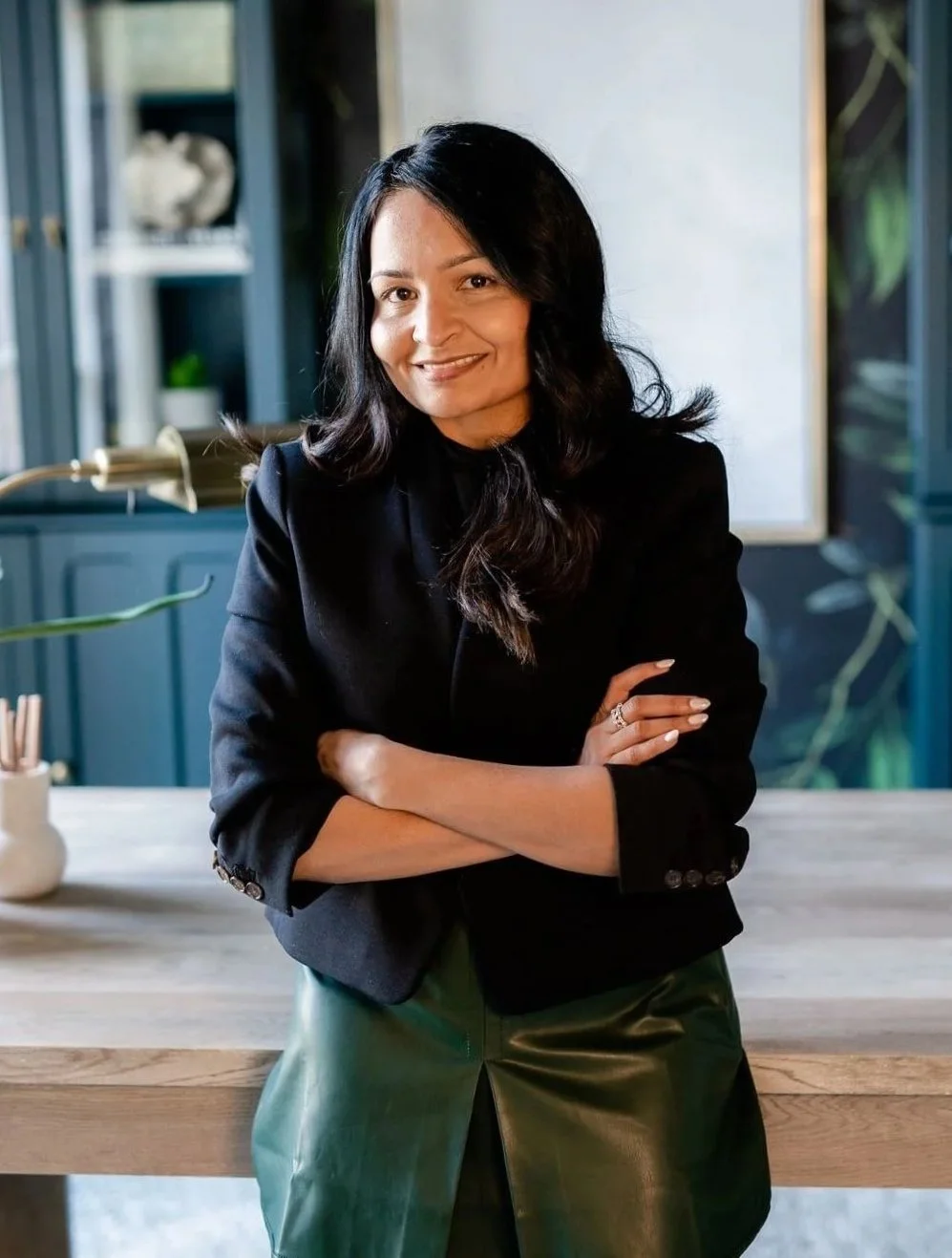 Jasmine Shah, luxury event planner and founder of The Velvet Finch, smiling with arms crossed in a black blazer and green skirt in a styled studio space