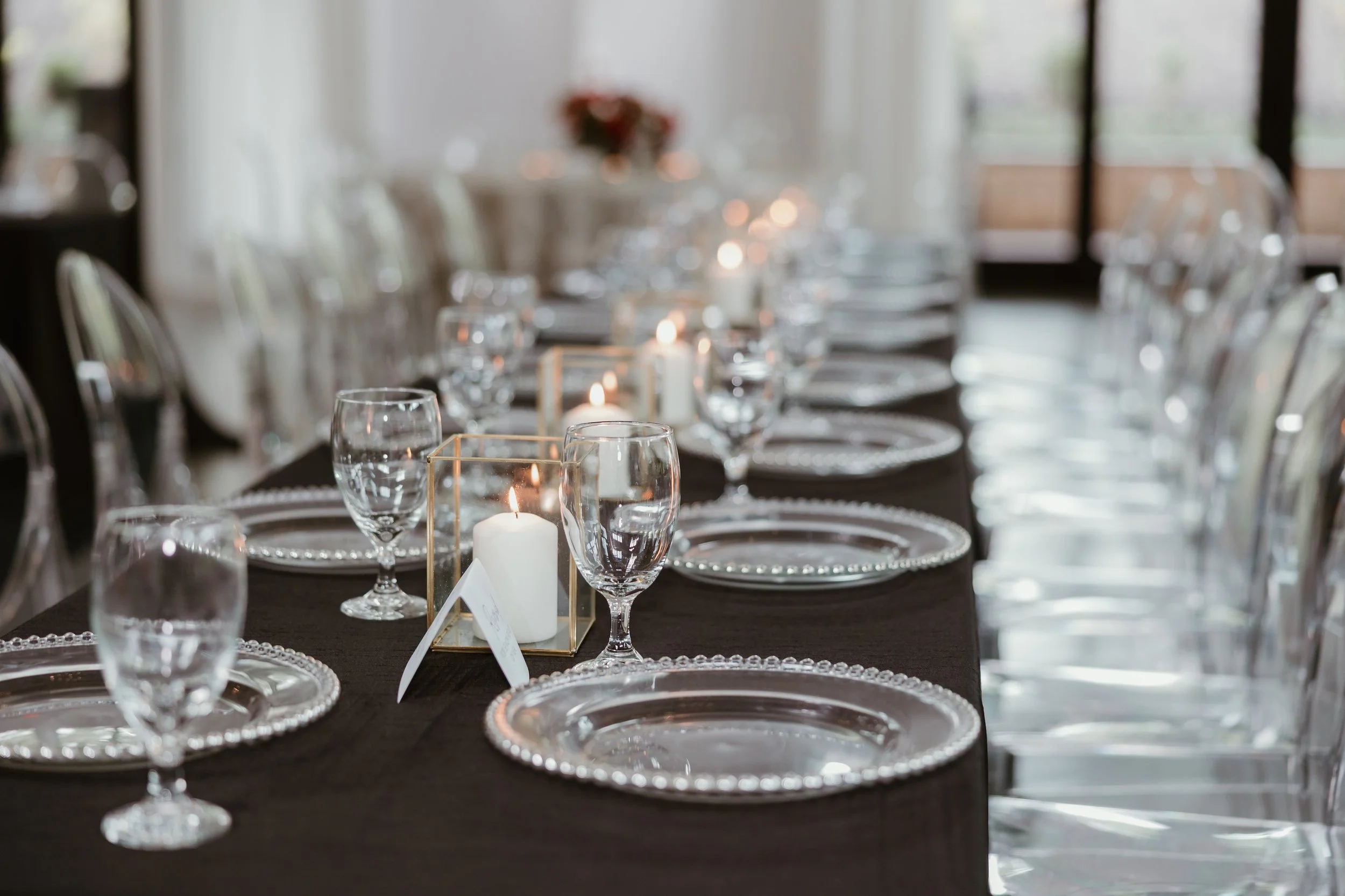Elegant candlelit event tablescape with crystal glassware, silver charger plates, and gold geometric candle holders on a dark linen tablecloth