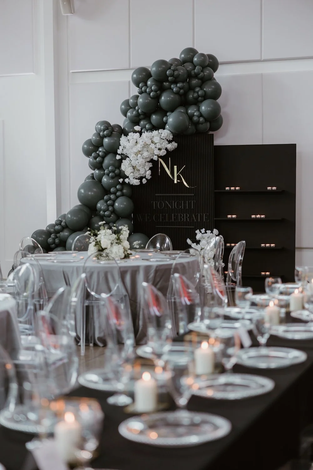 Elegant event setup with sage green balloon garland, crystal chandelier, and candlelit tables