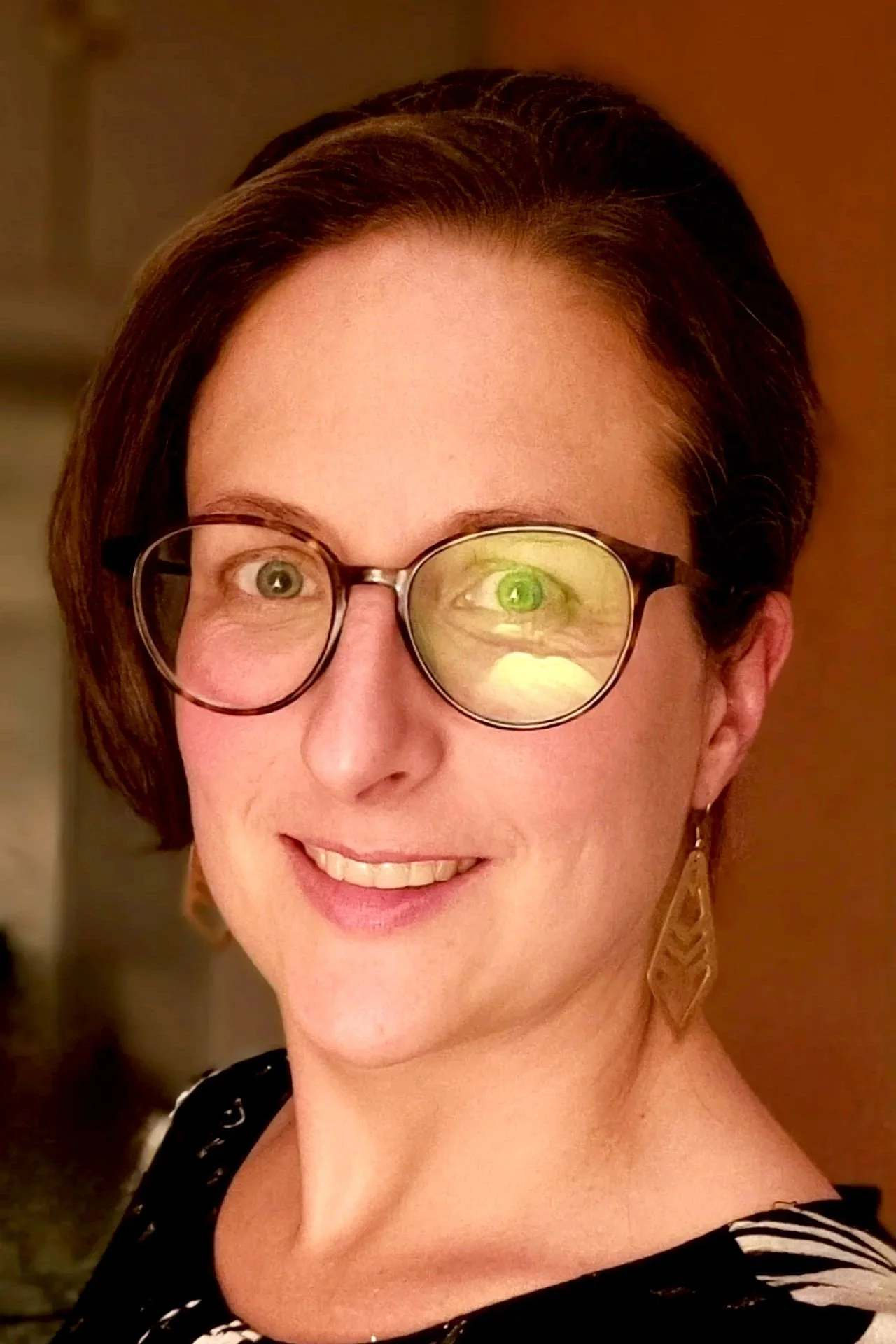 Photo of a white women with brown hair wearing glasses who is smiling and looking directly towards the camera
