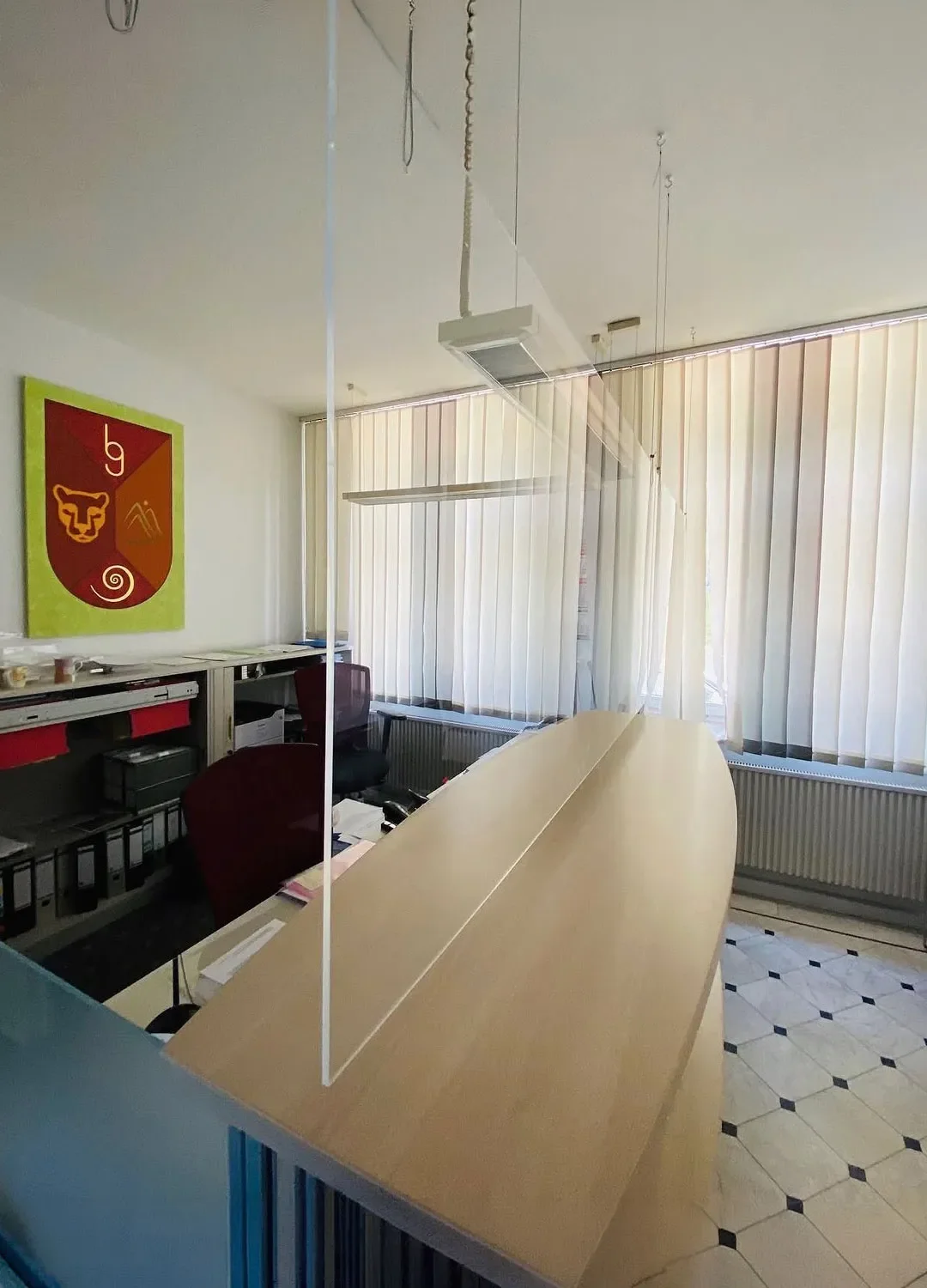 Transparenter Spuckschutz aus hochwertigem Plexiglas (Acrylglas), der als hängende Trennwand über einem Empfangstresen in einem Büro installiert ist.