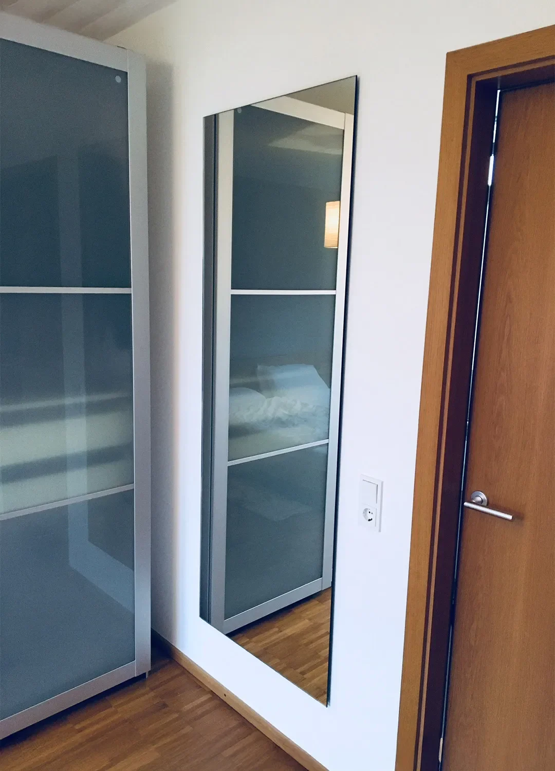 Maßgefertigter, rahmenloser Ganzkörperspiegel, der bündig an einer weißen Wand neben einer Holztür montiert ist und den Wohnraum optisch vergrößert.