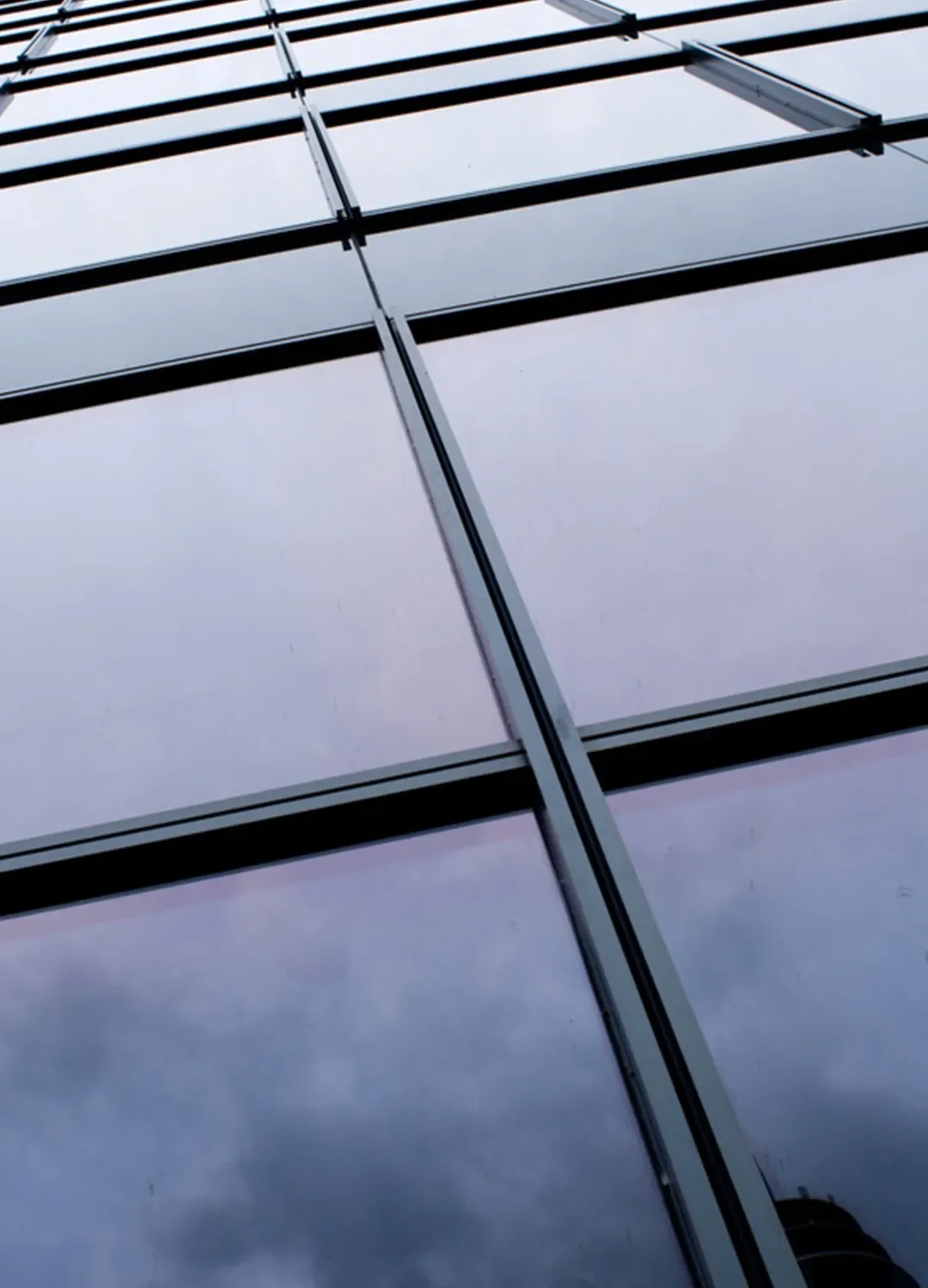 Nahaufnahme einer modernen Glasfassade mit hochwertiger Isolierverglasung, in der sich der bewölkte Himmel spiegelt.