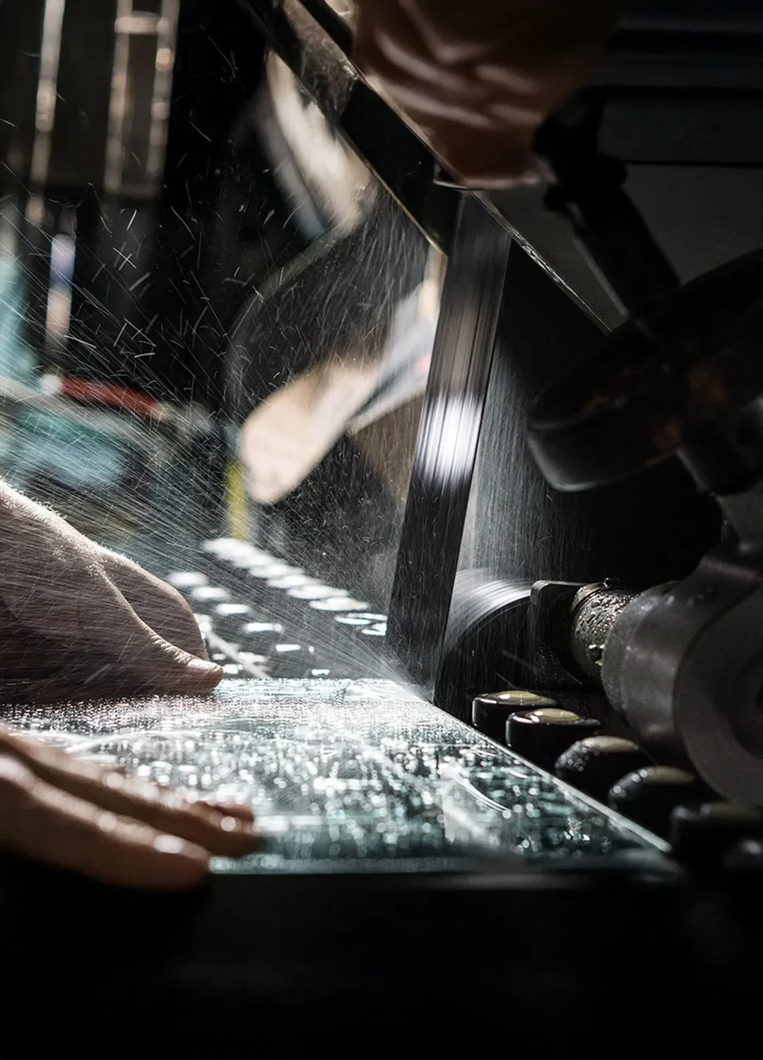 Präzise Kantenbearbeitung in der Glasschleiferei: Eine Glasscheibe wird unter Wasserkühlung maschinell geschliffen, während feiner Sprühnebel auf die Oberfläche trifft.