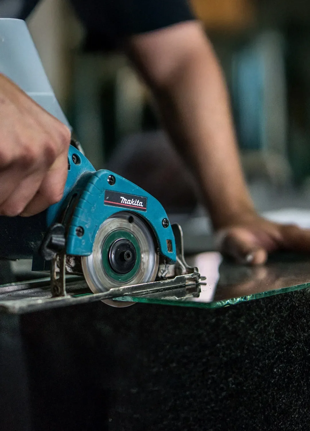 Präziser Glaszuschnitt in der Werkstatt: Ein Glaser schneidet eine dicke Glasscheibe mit einer spezialisierten Diamant-Glassäge für maßgefertigte Glaslösungen.