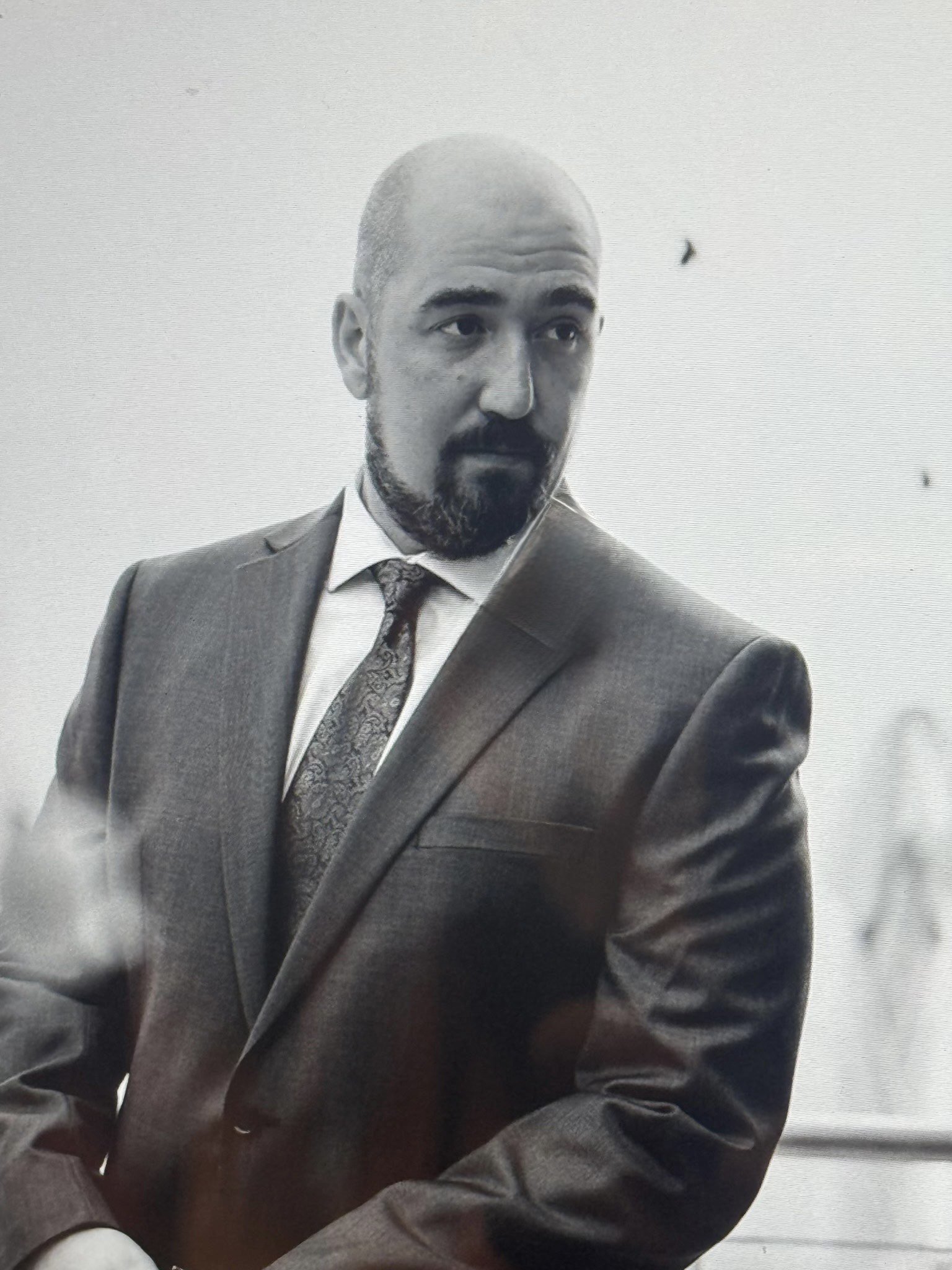 Black-and-white photo of a man in a suit and tie, with a bald head and beard, looking to the side.