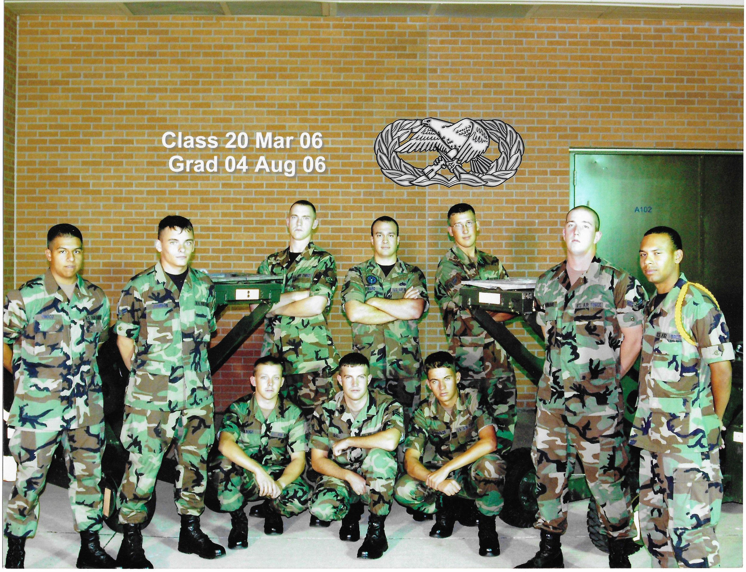 A group of military personnel in camouflage uniforms posing in front of a brick wall with a unit emblem. Text overlays indicate training completion dates in March and August 2006.