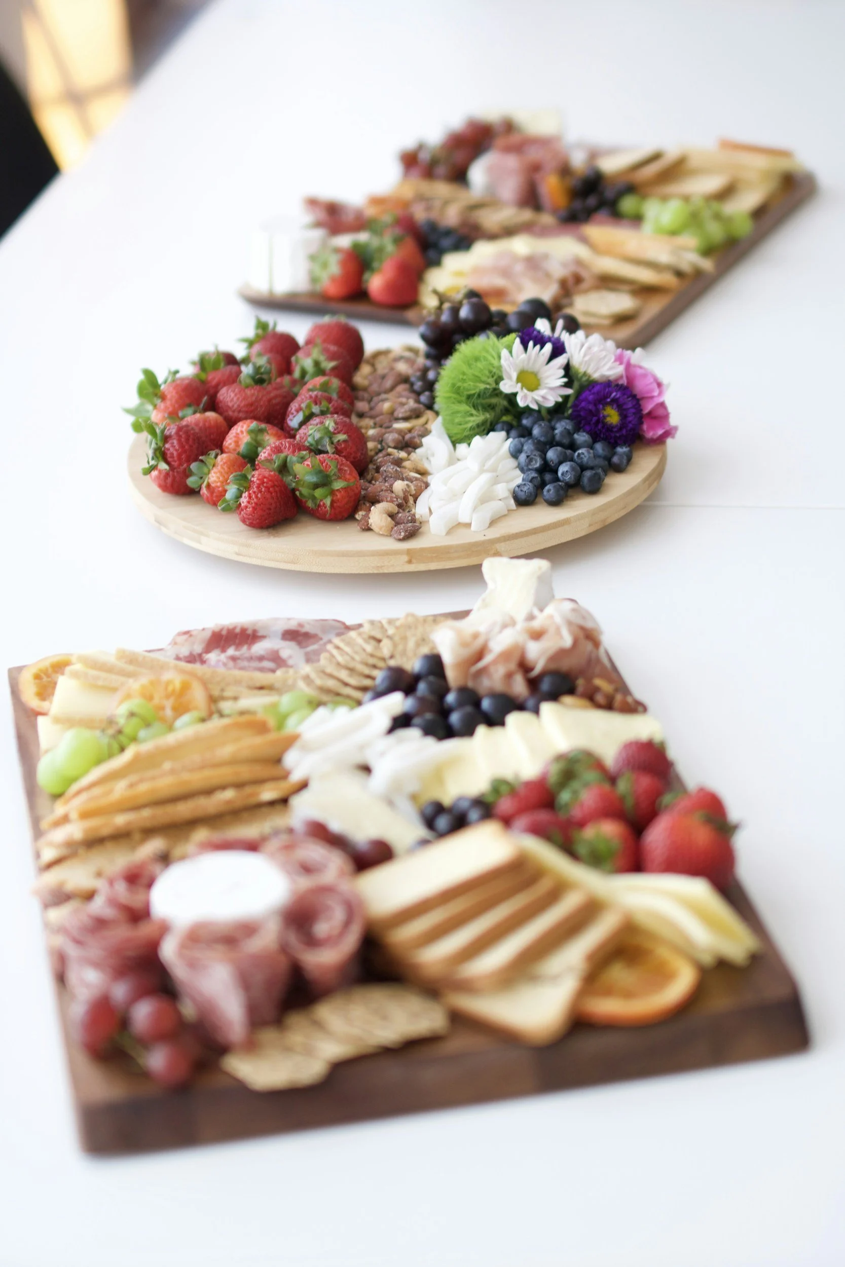 Charcuterie boards with strawberries, blueberries, grapes, cheese, crackers, and assorted meats on a white table.