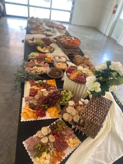 Charcuterie and cheese platter with fruits and snacks, decorated with white flowers on a long table.