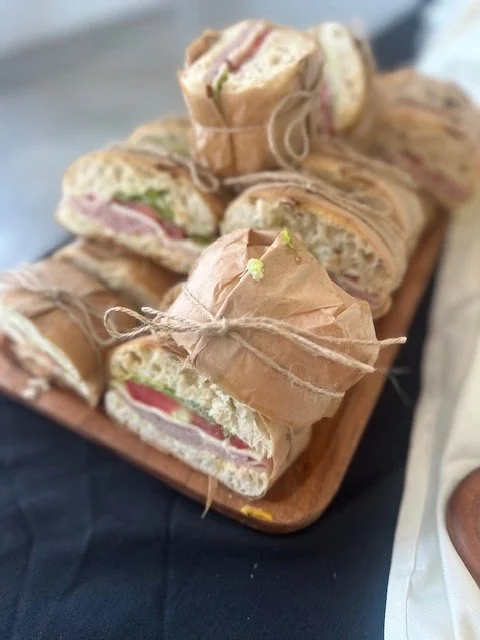 Sandwiches wrapped in brown paper and tied with string on a wooden tray.