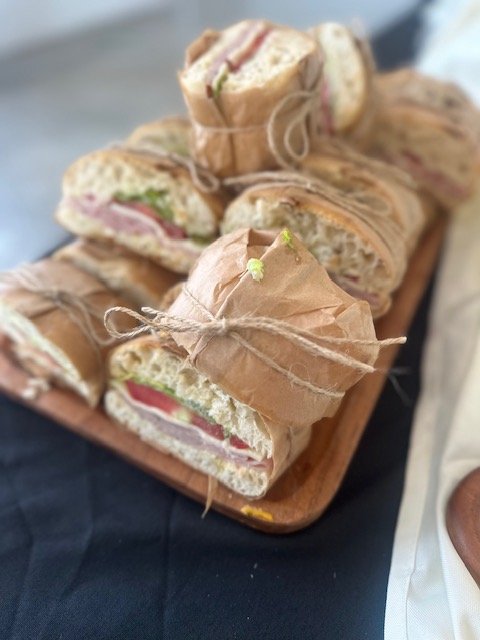 Sandwiches wrapped in brown paper tied with string, served on a wooden tray