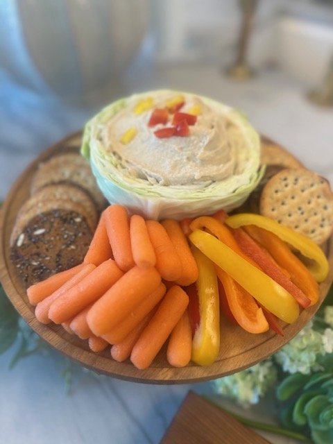 A wooden platter with veggies and snacks including baby carrots, sliced yellow and red bell peppers, a sandwich with lettuce and tomato, chocolate and peanut butter cookies, and an oatmeal cracker.