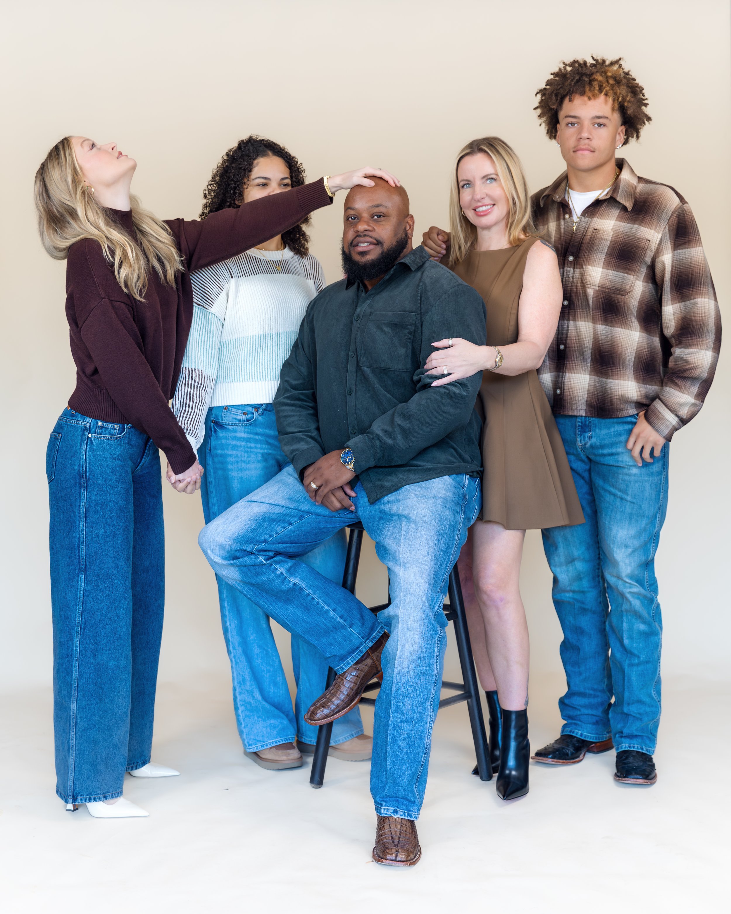 Group of five diverse people standing and sitting together, with four women and one man, in a studio with a plain background.