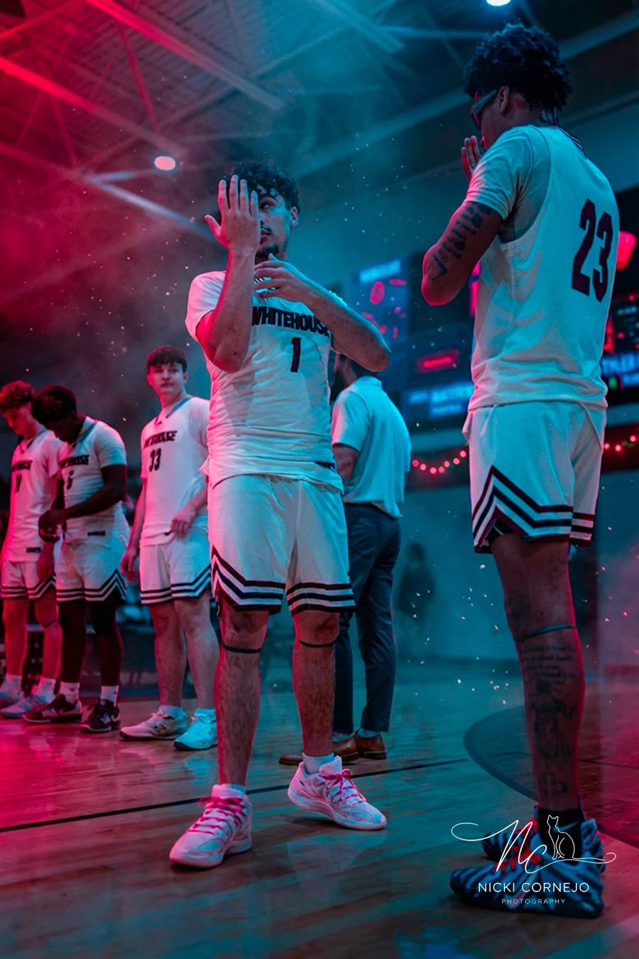 Basketball players standing in a line on the court during a game or ceremony inside a gym, with colorful lighting.