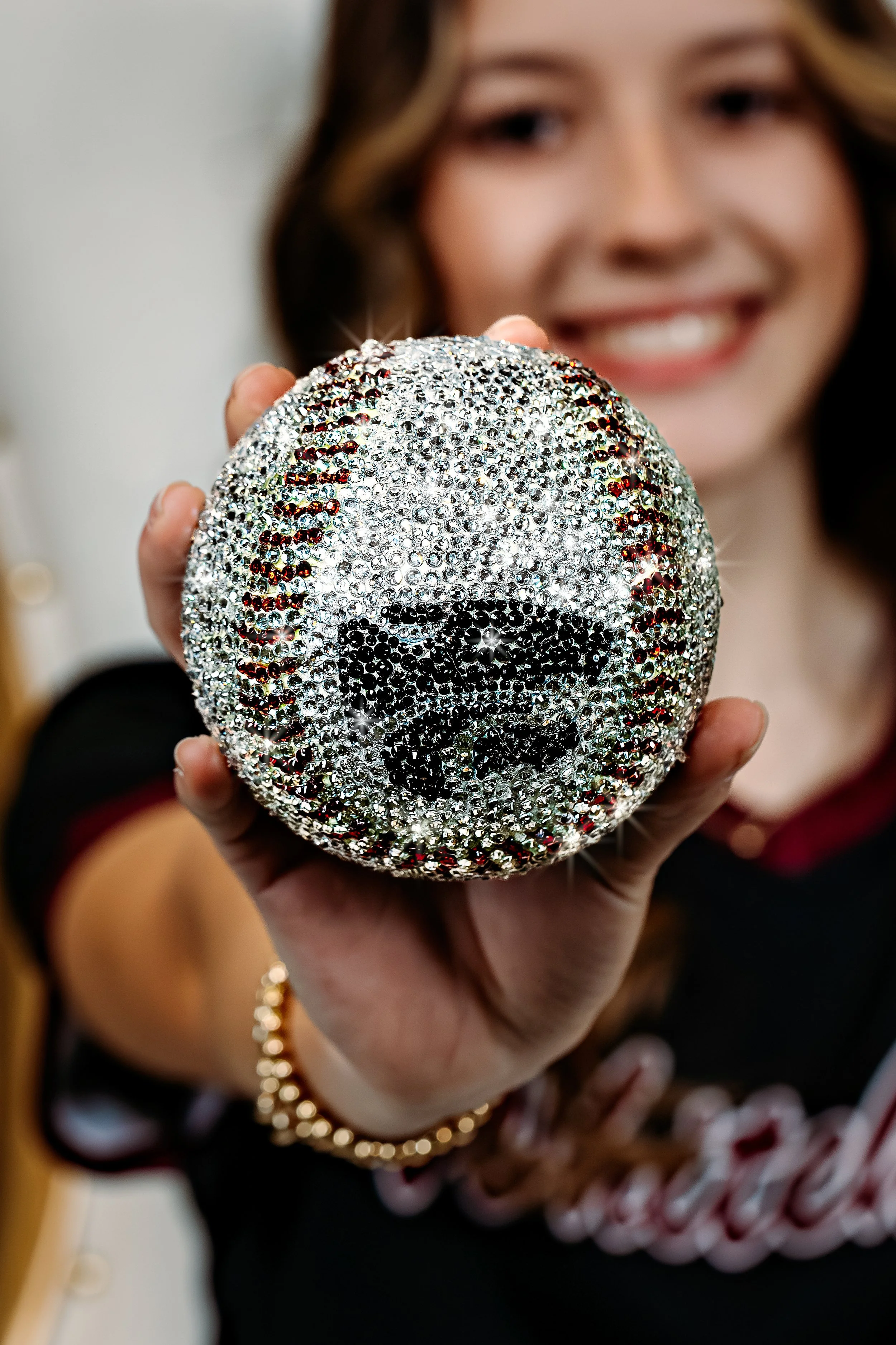 A woman smiling and holding a shiny baseball resembling a dog, covered in rhinestones.