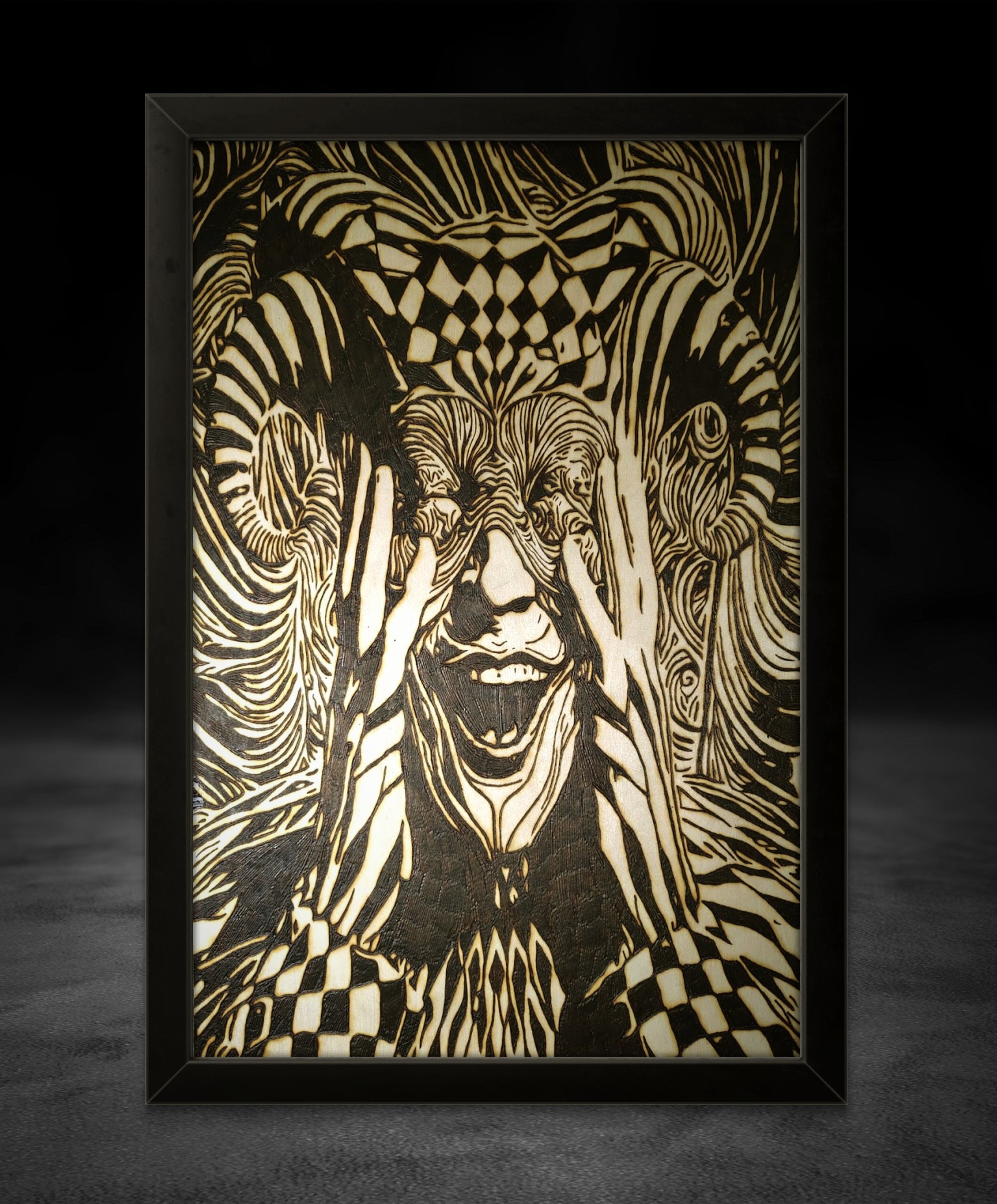 Framed wood burning artwork showing an abstract figure clutching its face, symbolizing chaos and fractured identity