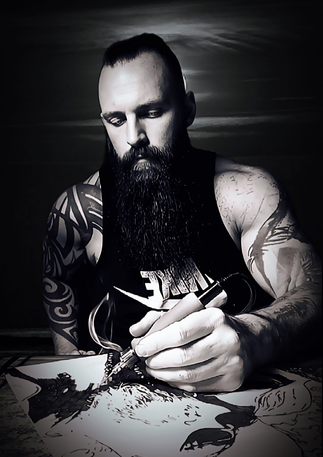 Black-and-white image of a tattooed artist actively wood burning a custom artwork, capturing the handcrafted pyrography process and focused detail work on natural wood surface
