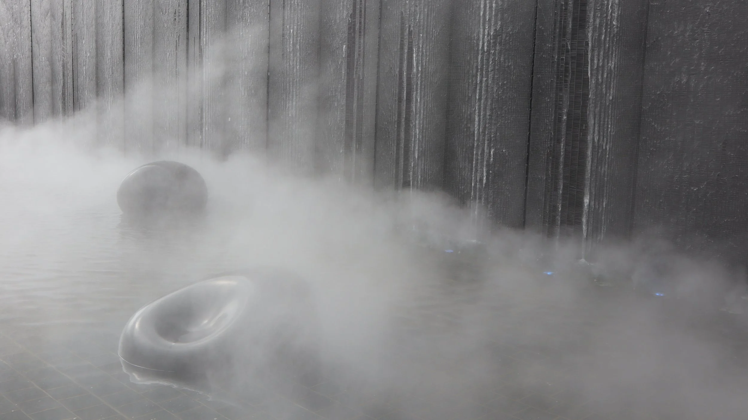 Sistema de inodoros en un baño con vapor y paredes de mármol oscuro.