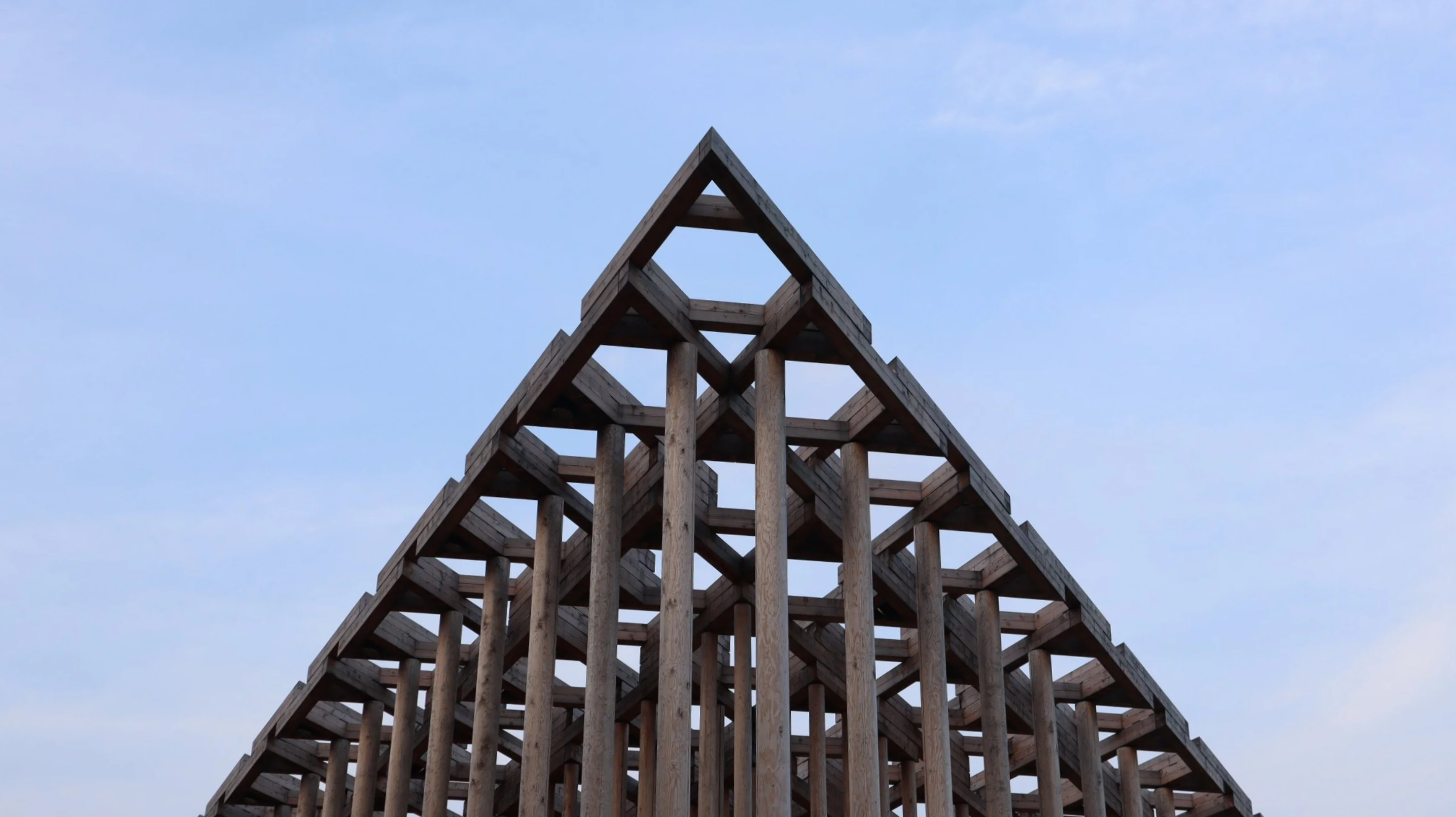 Estructura de madera con forma de pirámide contra el cielo azul.
