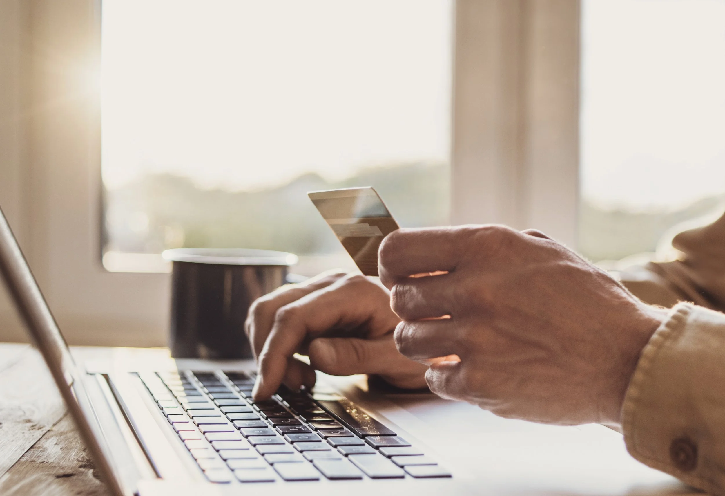 Person using a laptop and holding a smartphone near a window.