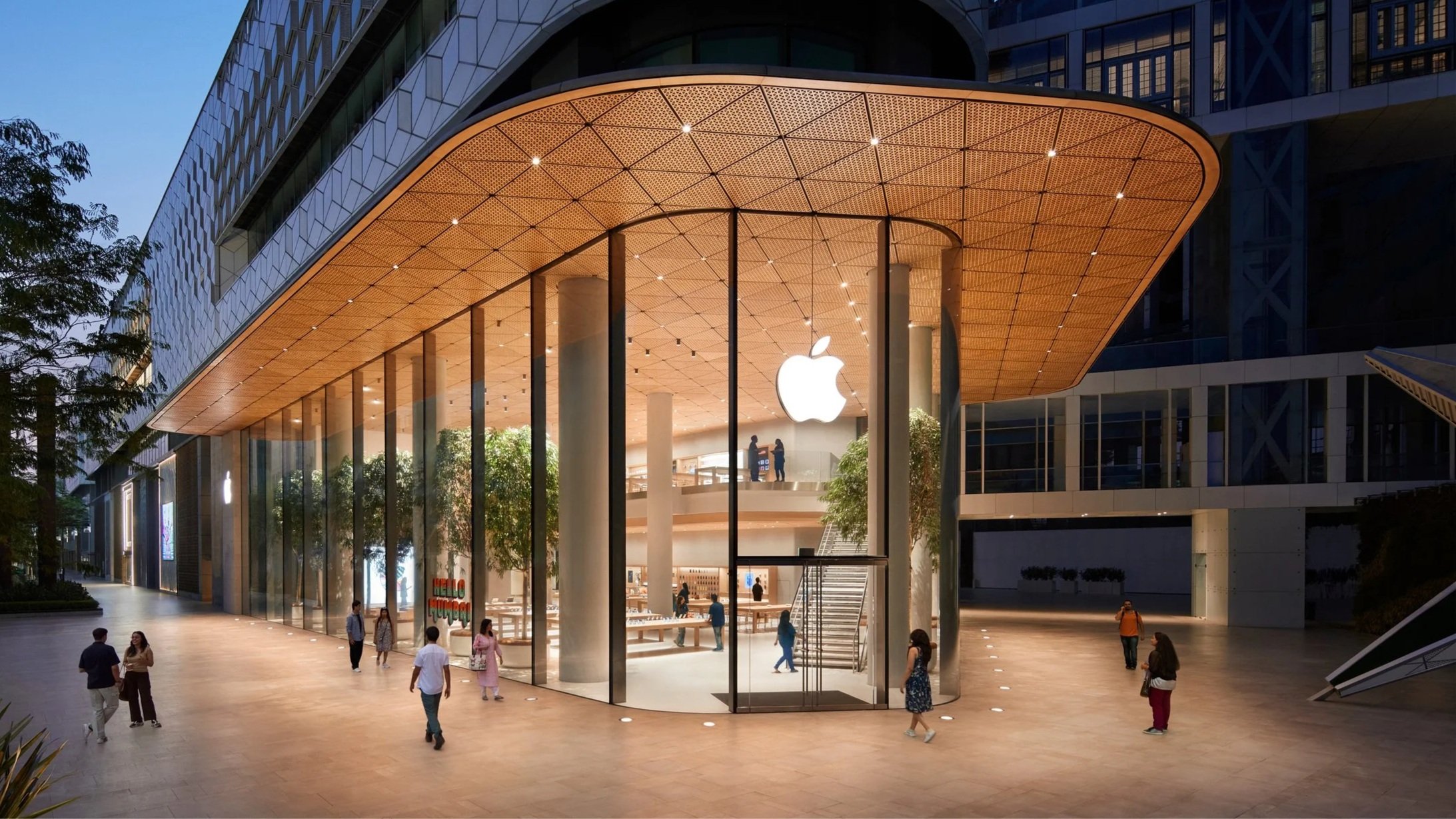 Apple store exterior with illuminated apple logo and blurred moving taxis in front.