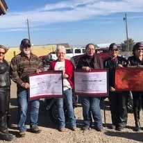 Five people standing outdoors, holding certificates or awards, with a clear sky and some utility poles in the background.