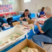 People assembling or packing food items at a table with boxes and supplies in a community service setting.