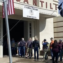 People standing outside the entrance of a building labeled 'Pentil,' with a flag and a banner above the door.