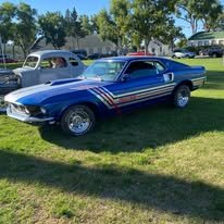A vintage blue car with red and white racing stripes parked on grass near other vehicles and trees.